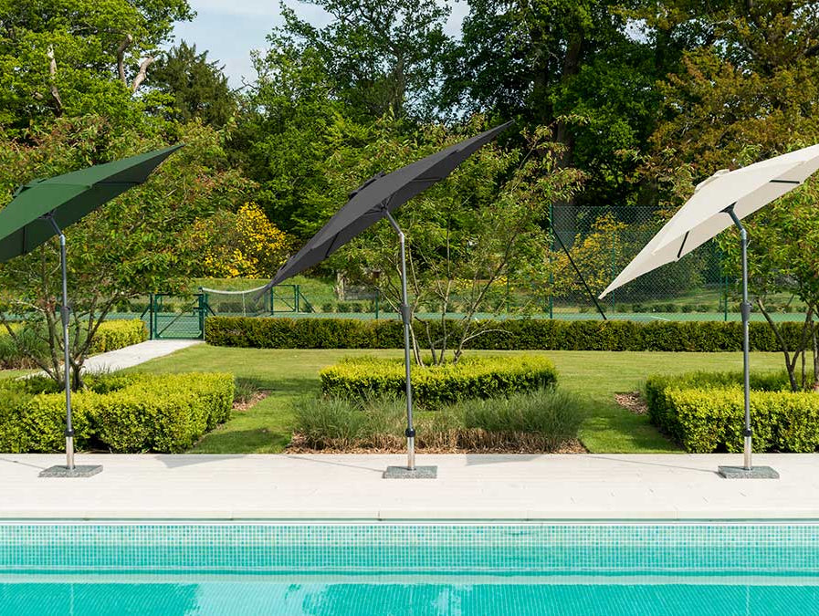Green, black and cream tilting parasols in front of a swimming pool