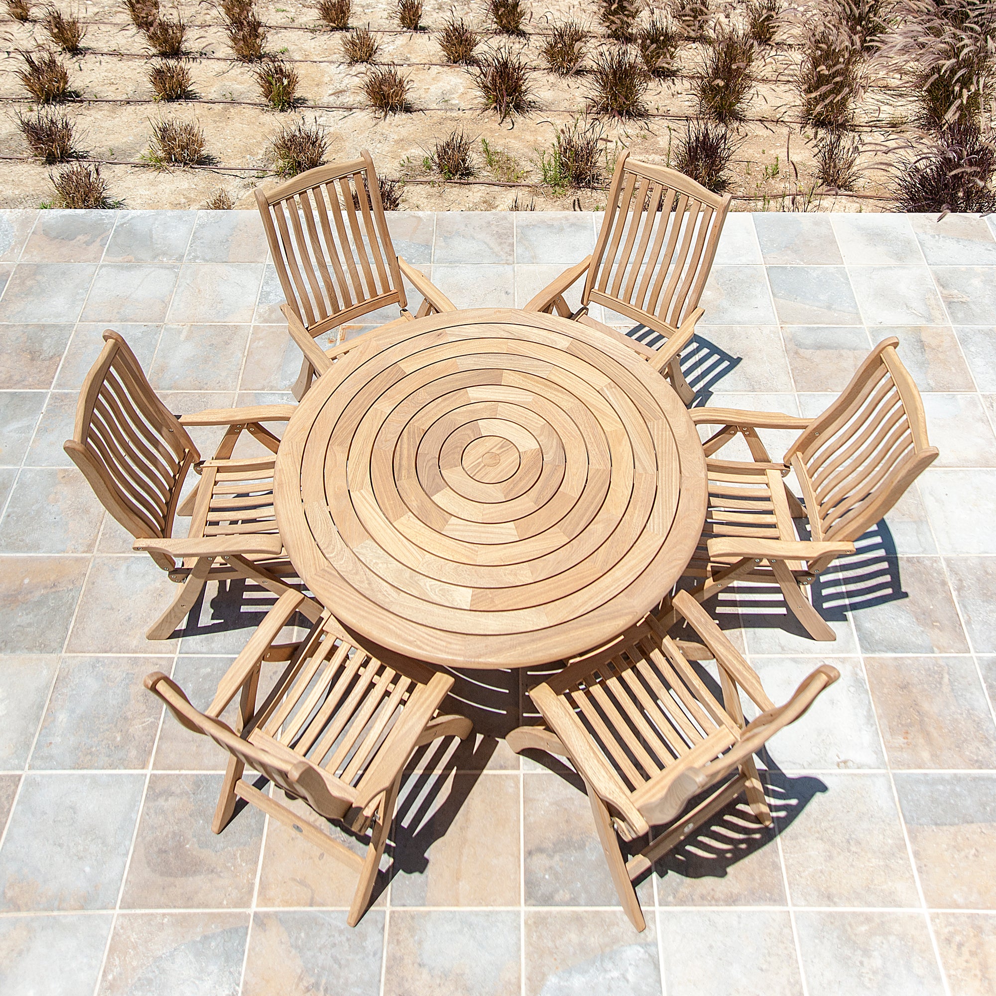 Wooden outdoor dining set with a round table and six chairs on a tiled patio.