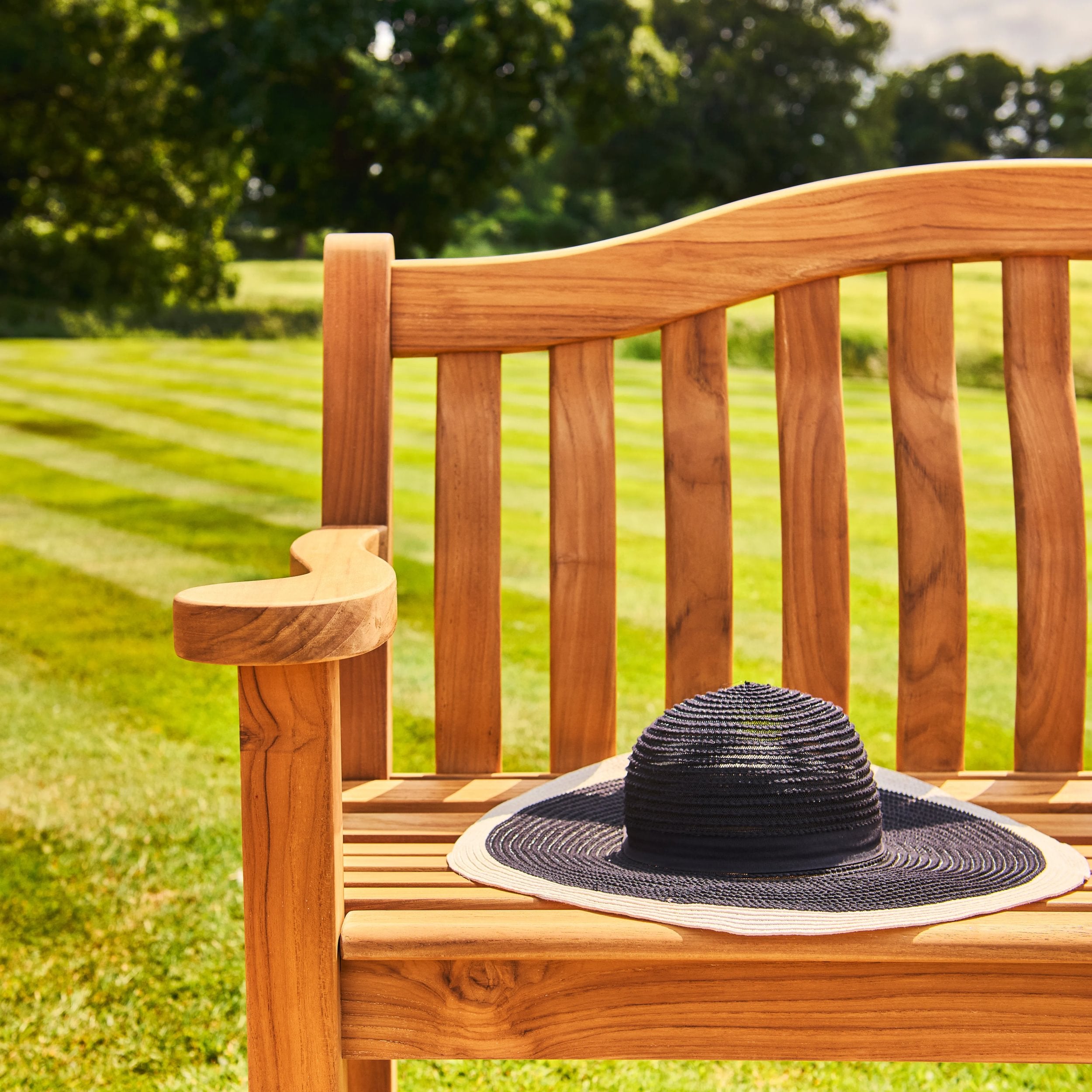 woven black straw hat on a wooden bench in a field background