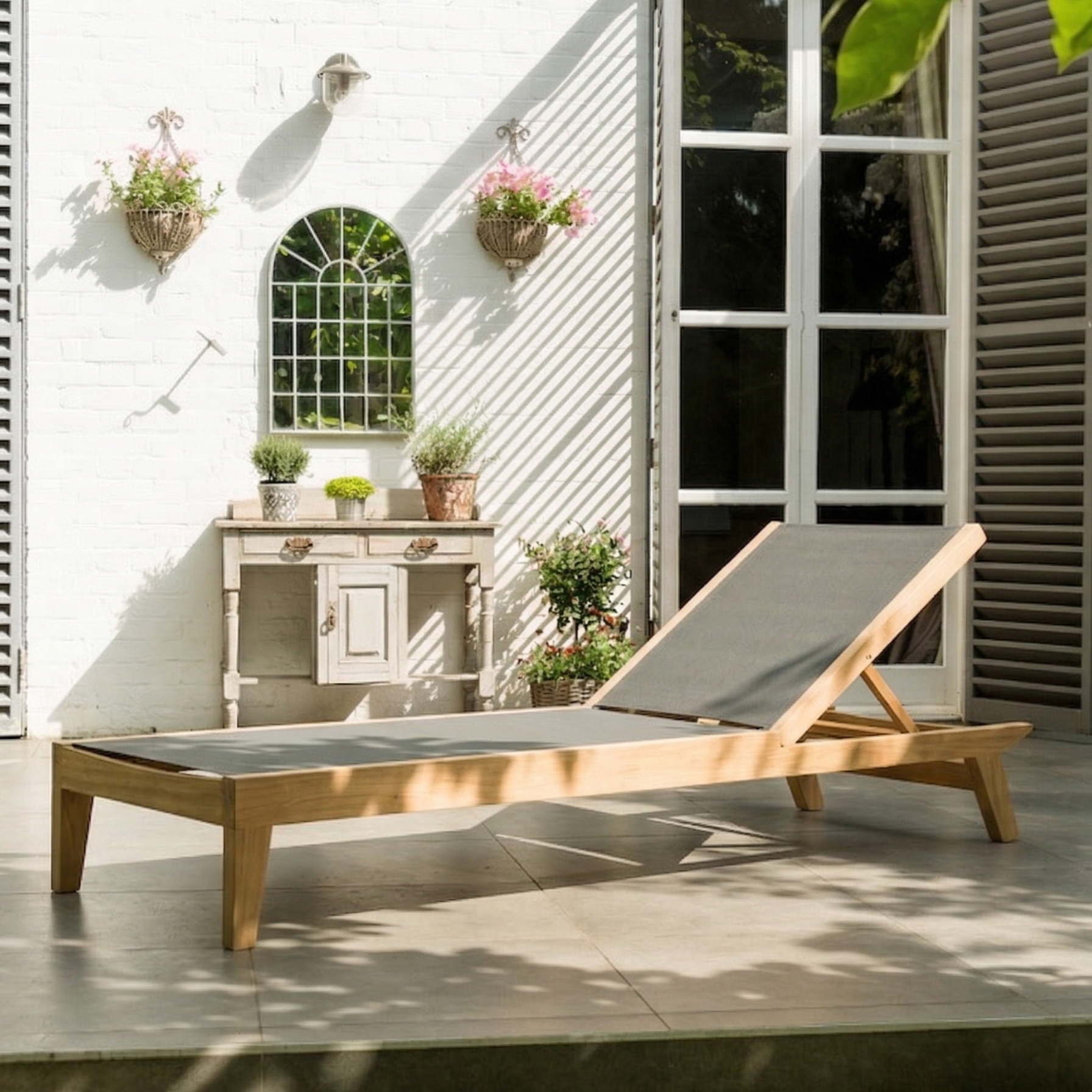 Wooden sun lounger on a patio with a white building and plants in the background