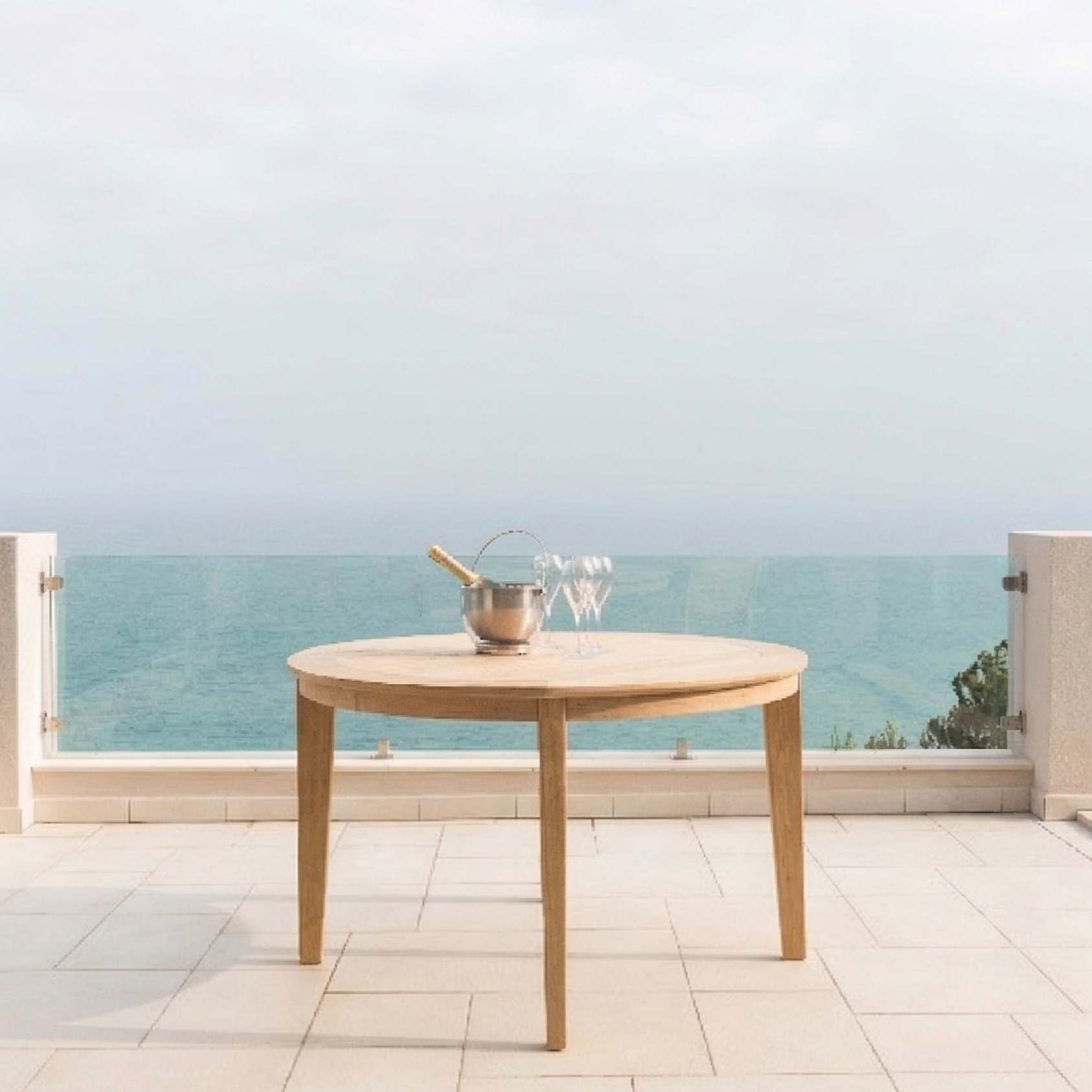 roble round table on a patio with champagne and glasses and the sea in the background