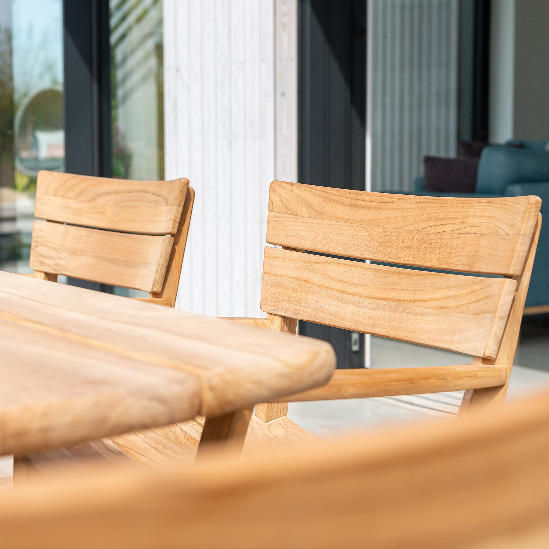Wooden outdoor table and chairs with a blurred background of a modern house.