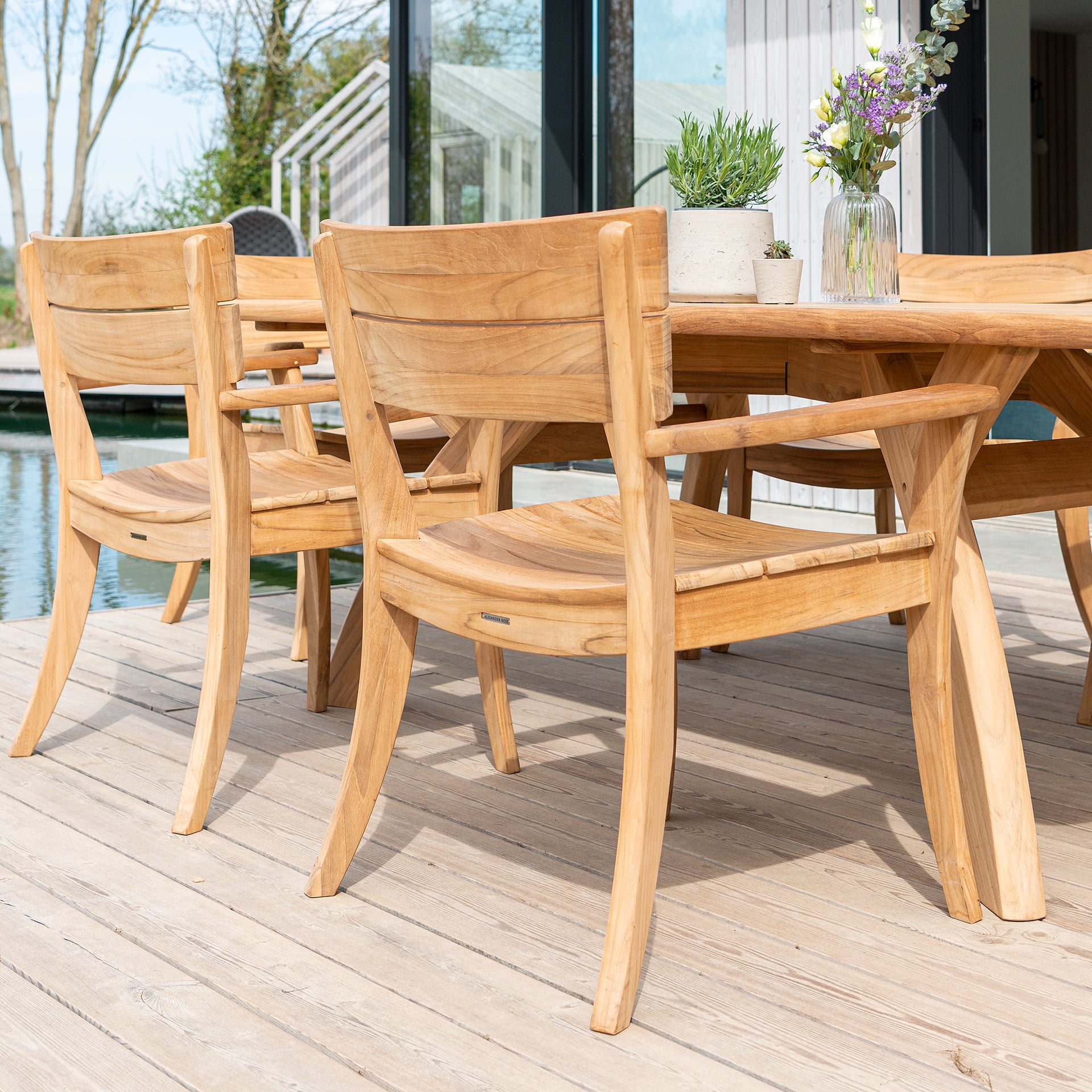 Wooden outdoor dining table and chairs on a deck with a pool in the background
