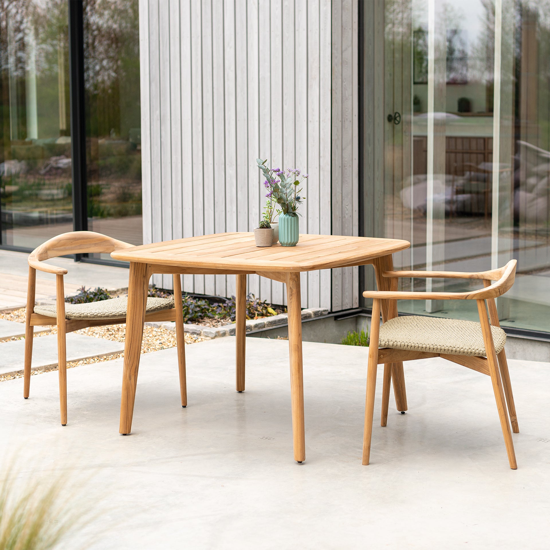 Square teak outdoor dining table and two curved dining armchairs