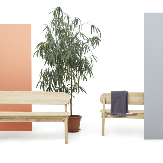 Two stylish pine benches with a potted plant between them against a white background.