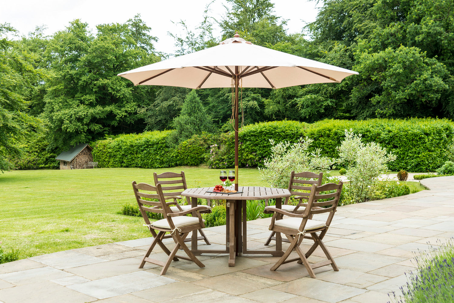 Outdoor patio set with table and chairs under a large umbrella in a garden setting.