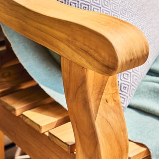 Close-up of a wooden chair with a light blue blanket and patterned cushion