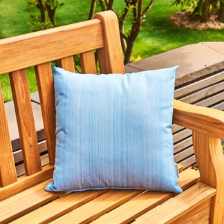 Blue pillow on a wooden bench with a green outdoor background