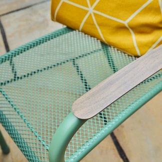 Close-up of a green metal chair with a yellow cushion on a tiled floor.