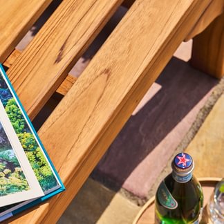 Close-up of a wooden table with a magazine and a bottle on a patio