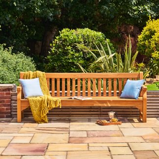Wooden bench with cushions and a blanket in a garden setting