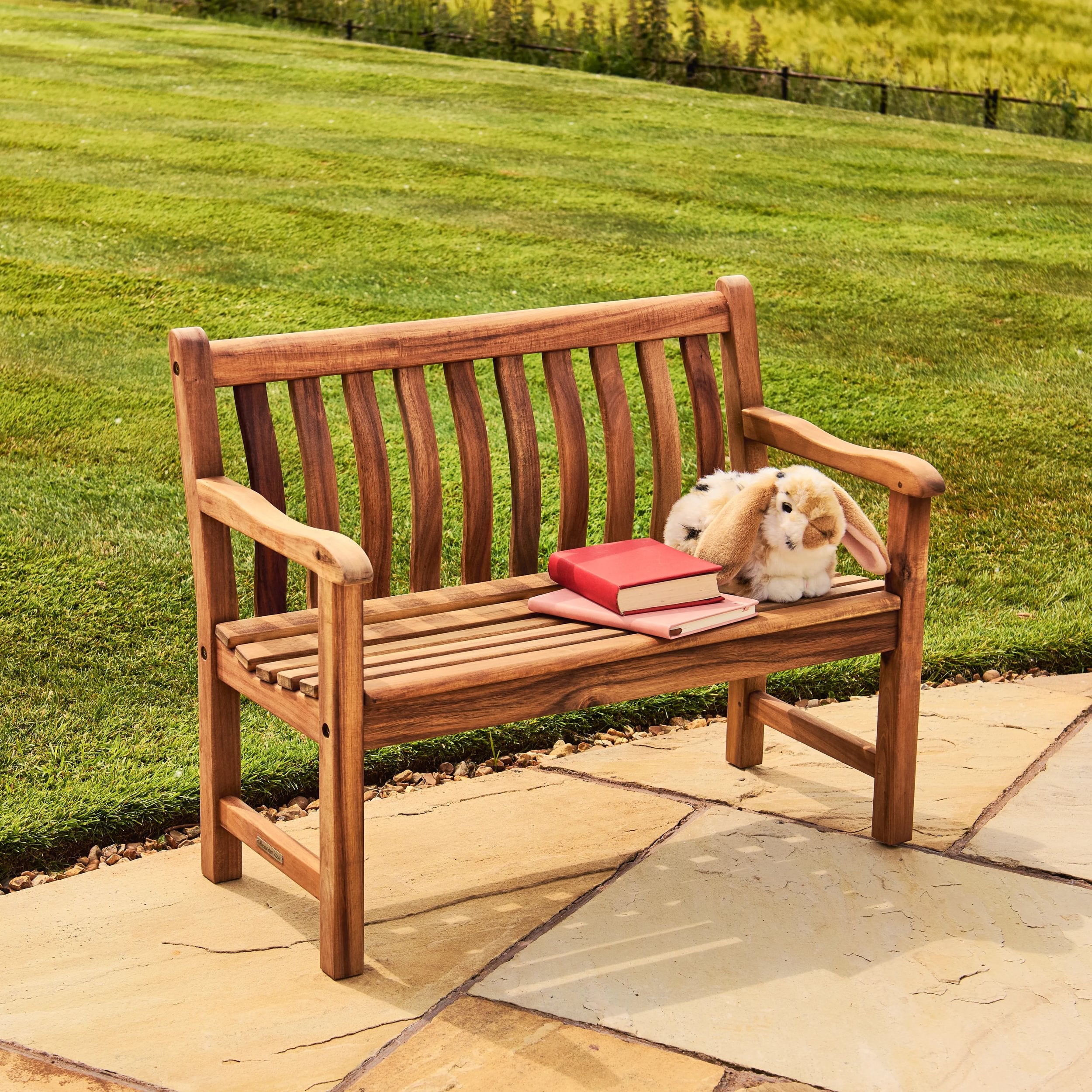 Wooden bench with a book and plush toy on a stone patio with grass in the background