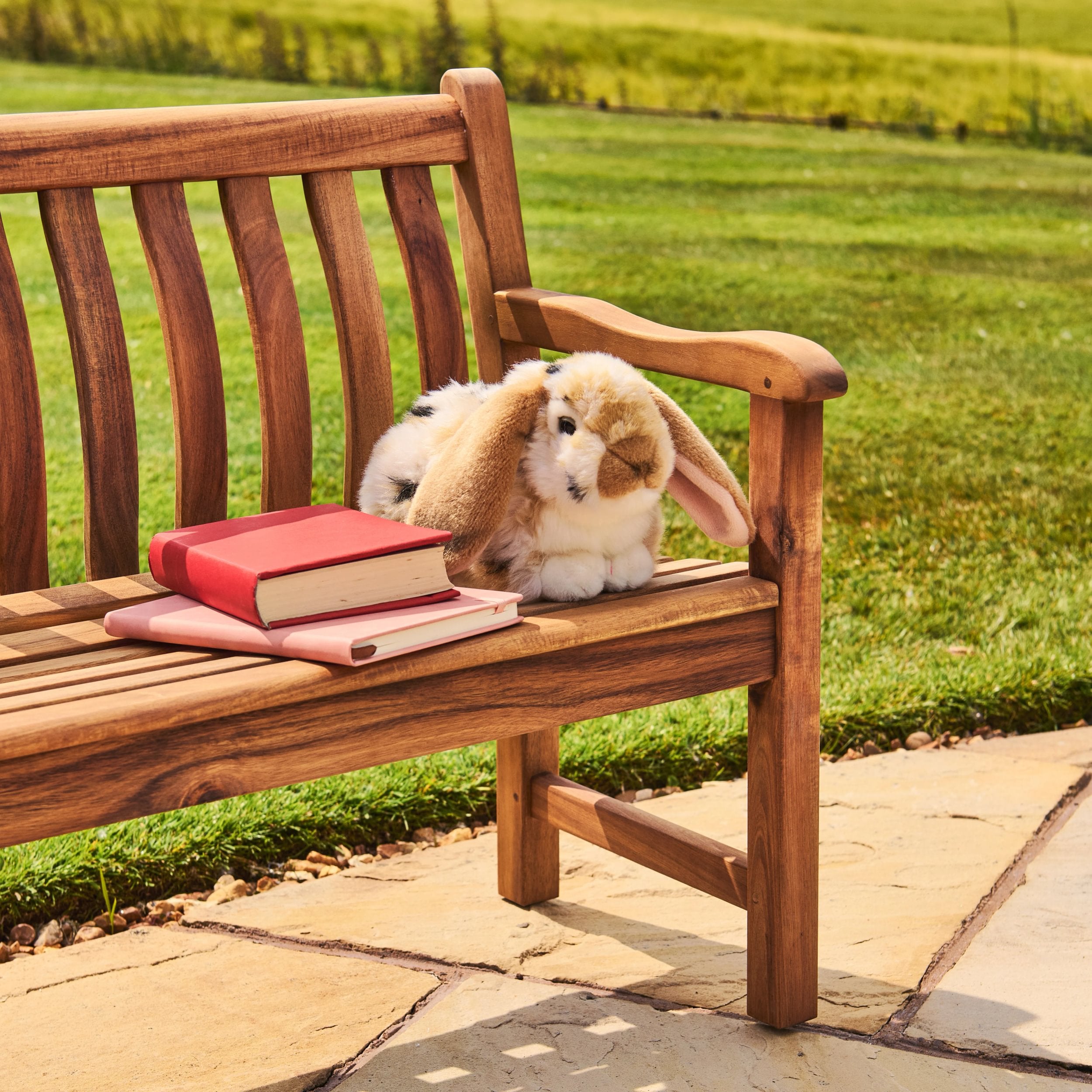 Wooden bench with a plush rabbit toy and books on a grassy outdoor setting