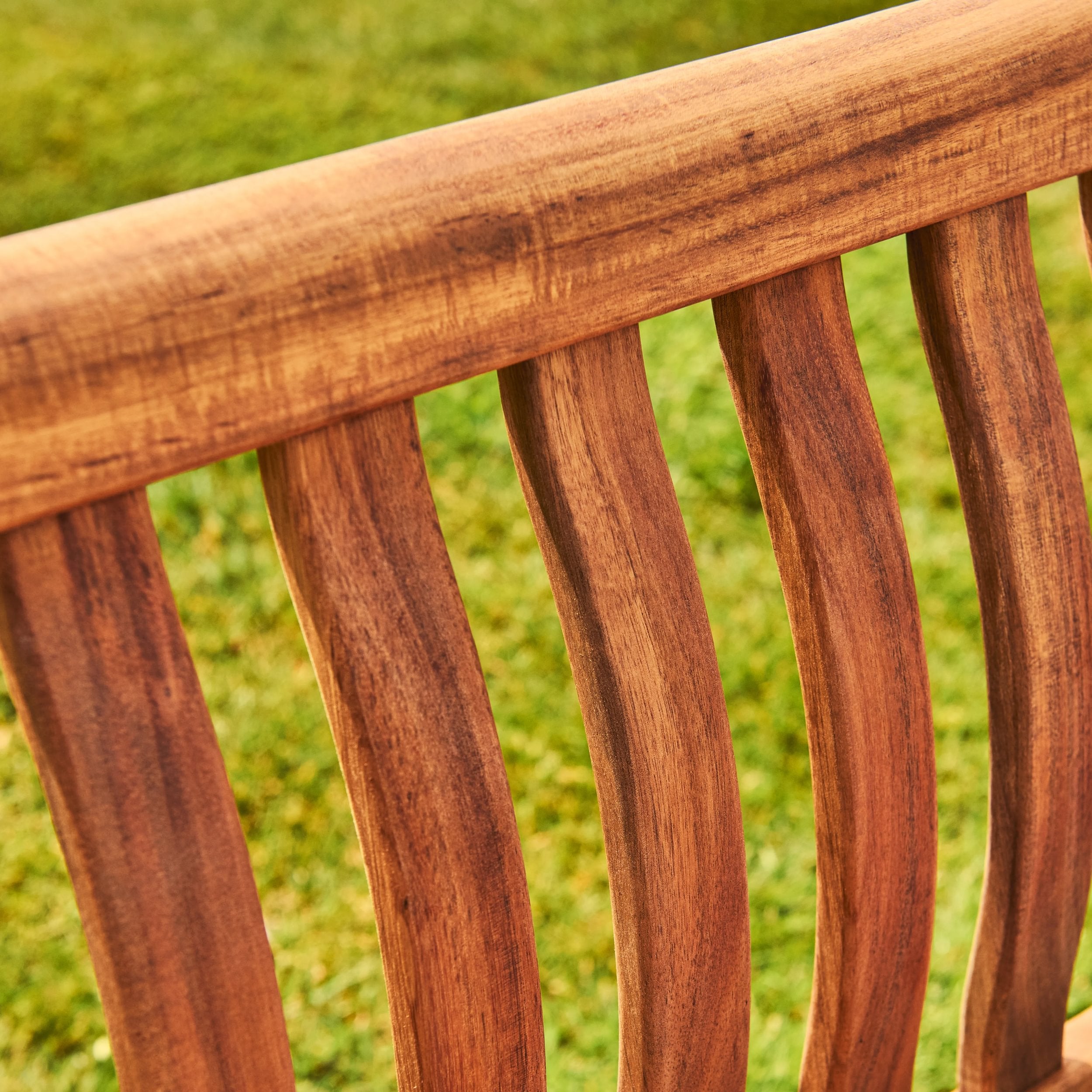 Close-up of a wooden bench with a blurred green grass background