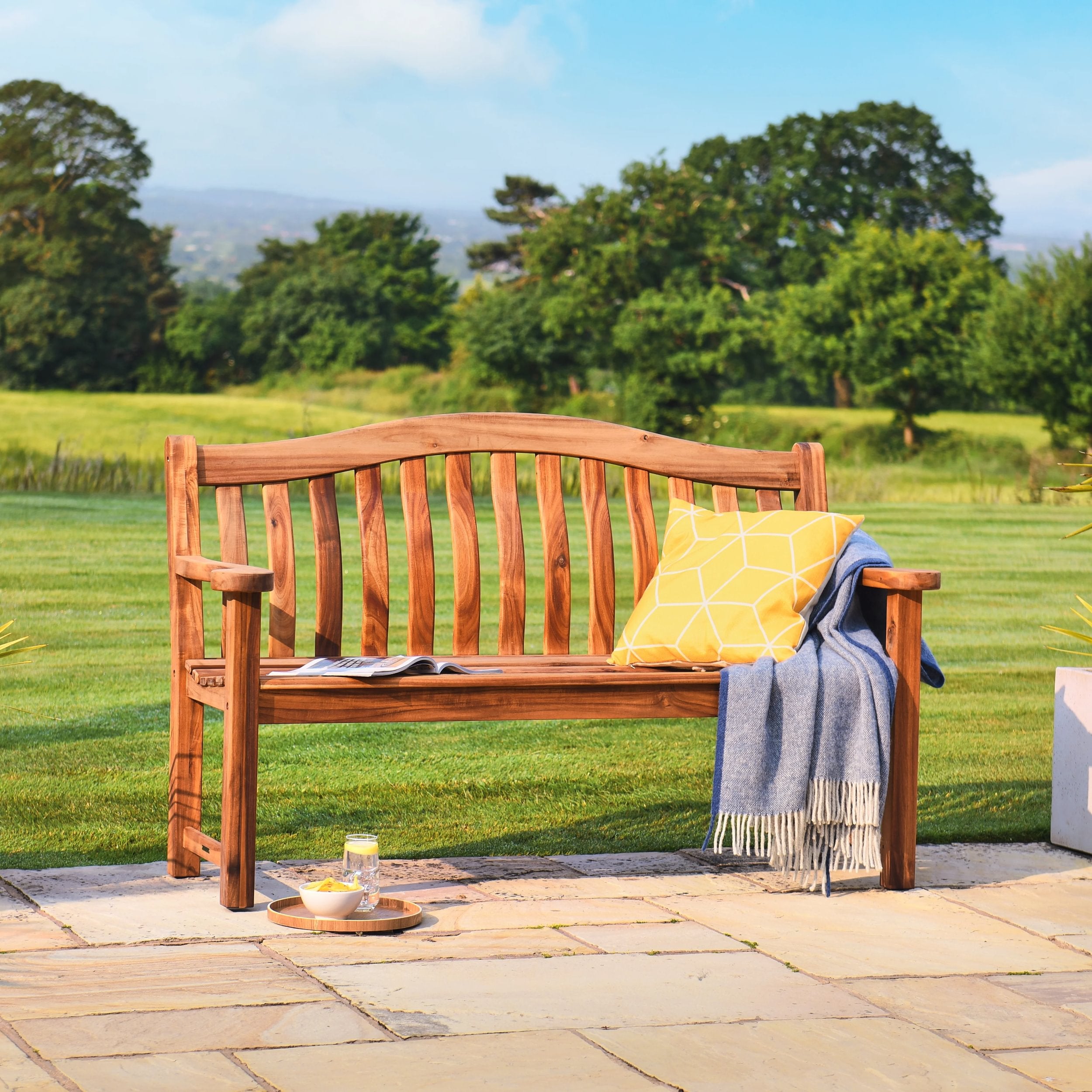 Wooden bench with a yellow cushion and blue blanket in a garden setting