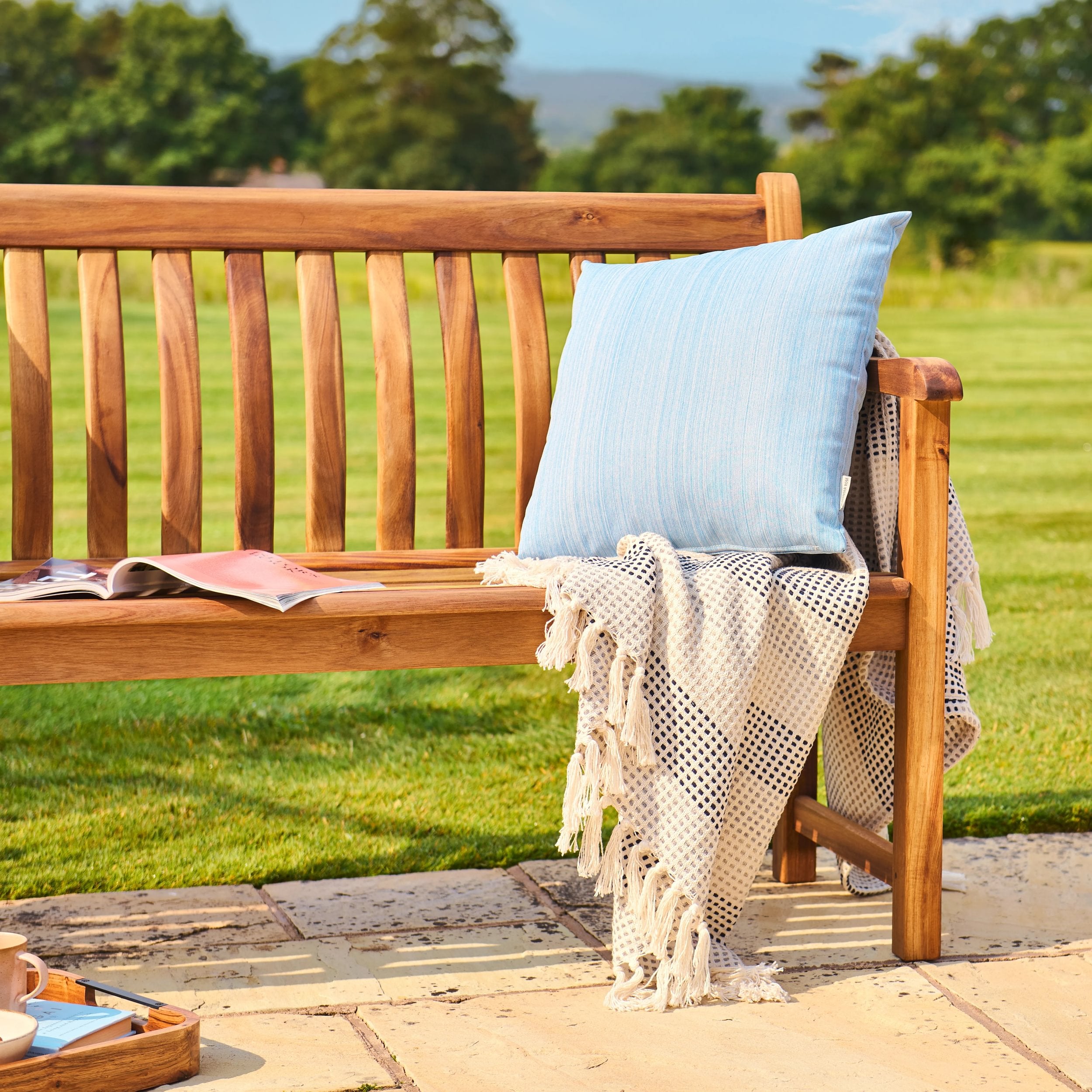 Wooden bench with a blue pillow and blanket on a patio
