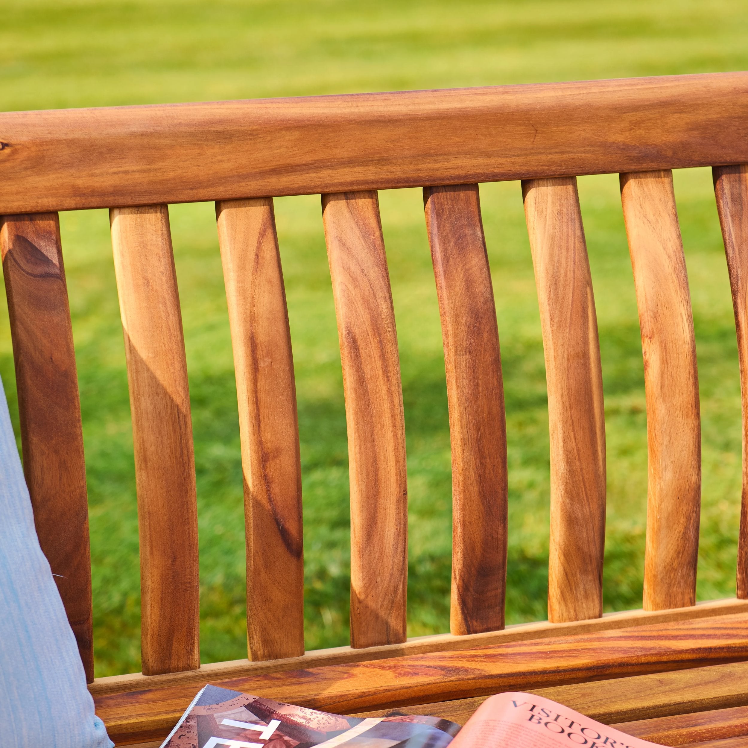 Wooden bench with a person reading a magazine against a grassy background