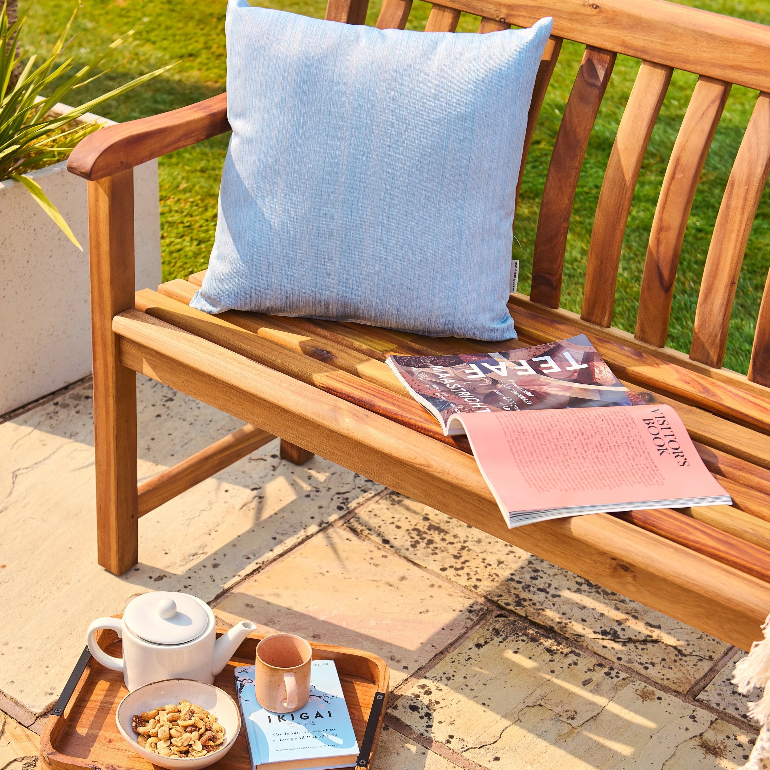 Wooden bench with a blue pillow, magazine, and snacks on a patio