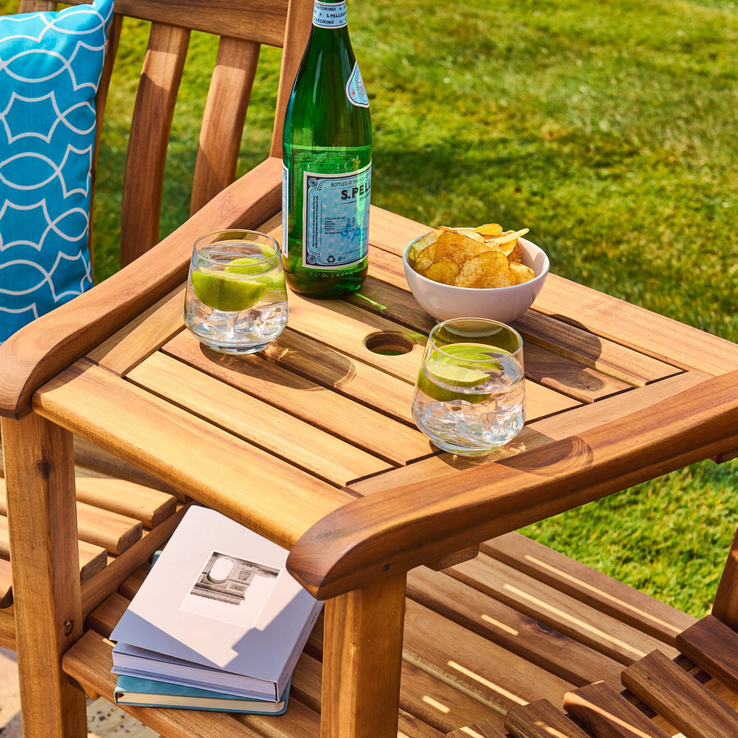 Wooden outdoor table with a bottle, glasses, and snacks on a grassy background