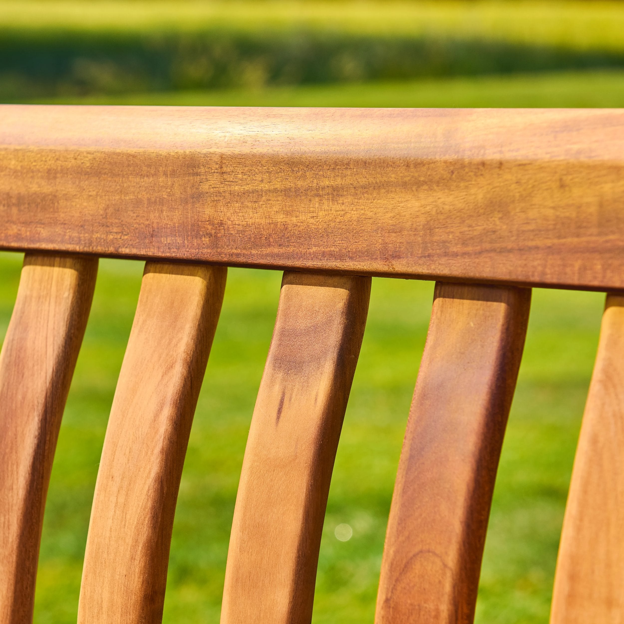 Close-up of a wooden bench back with a blurred green field background