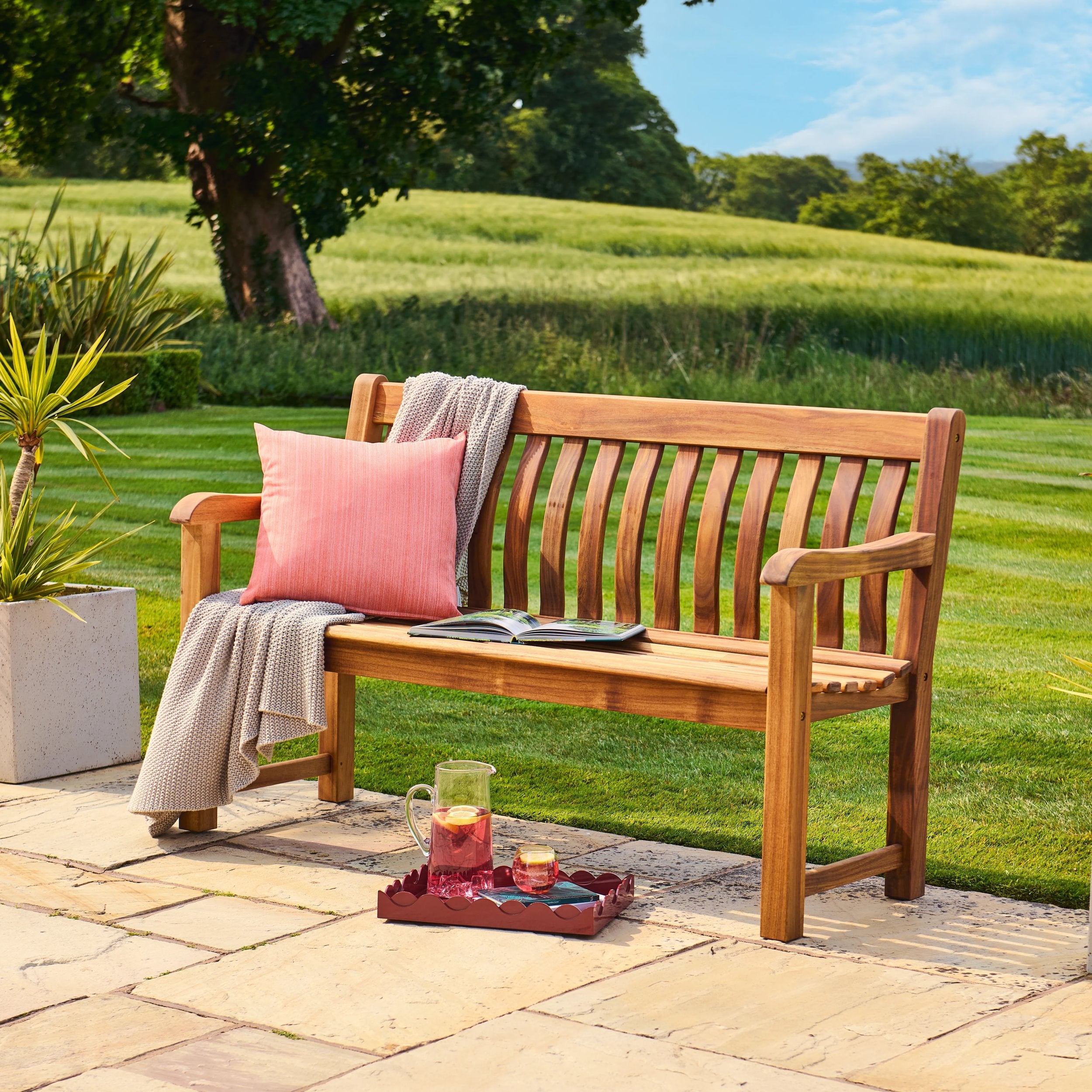 Wooden bench with pink cushion and tray of drinks on a patio