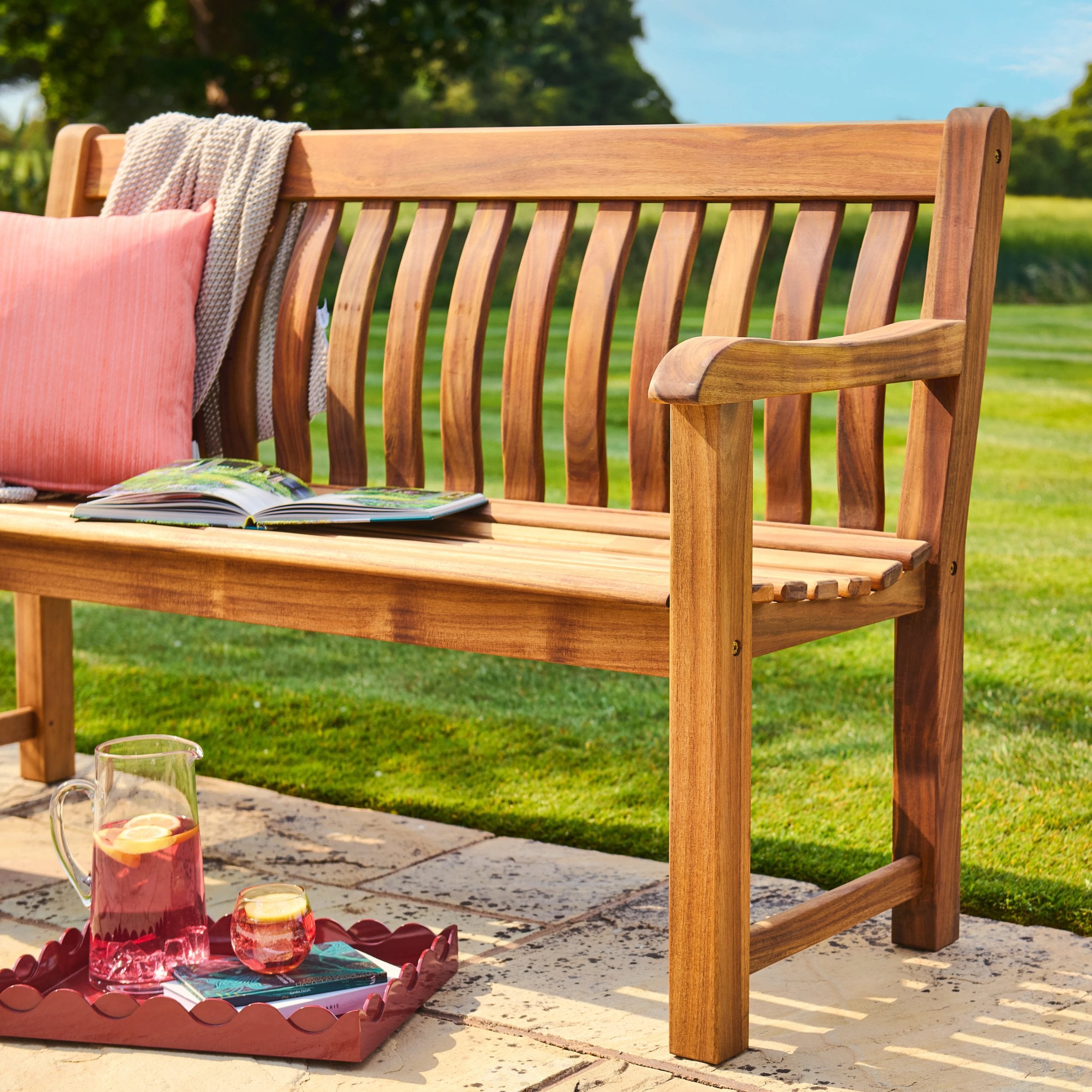 Wooden bench with pink cushion and tray of drinks on a patio