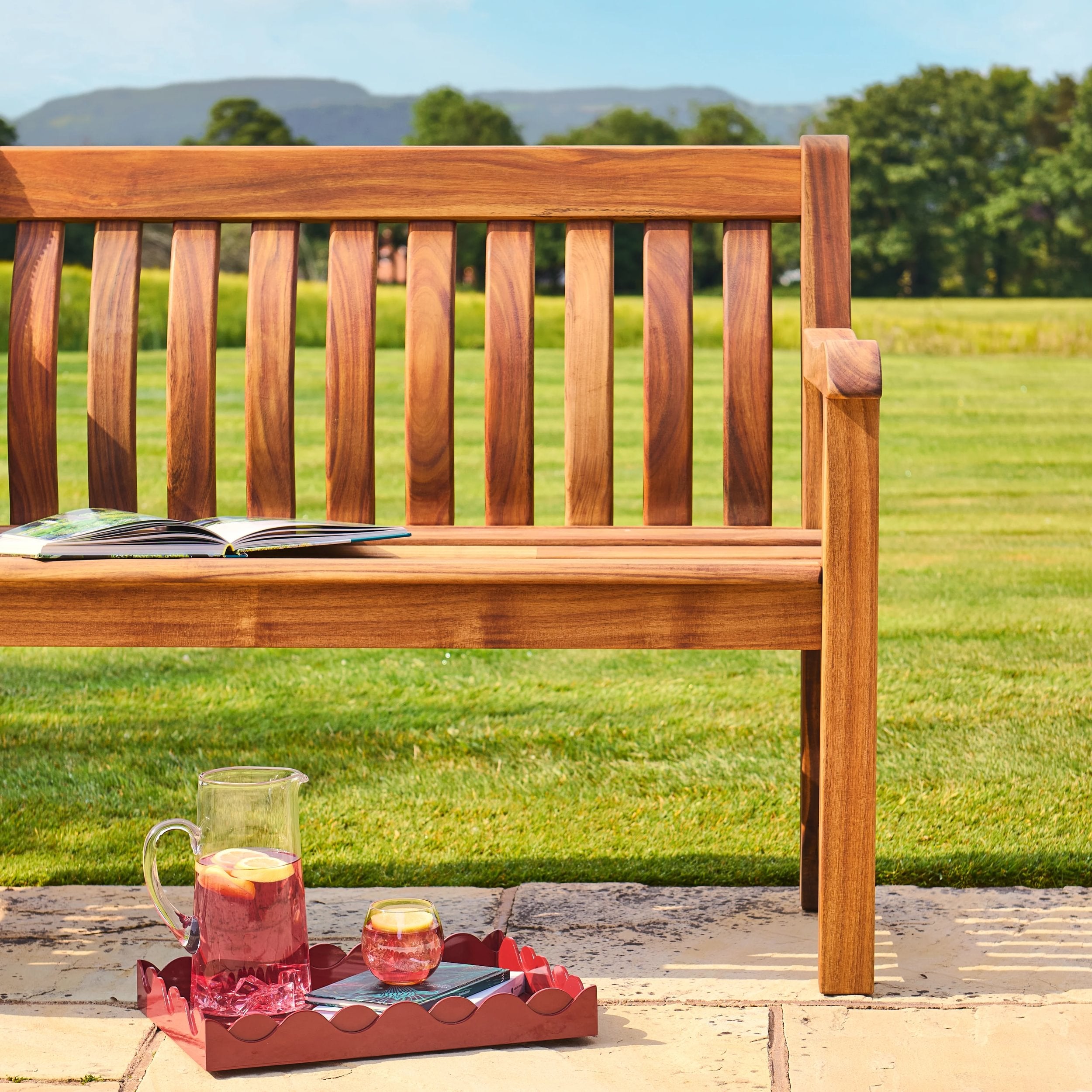 Wooden bench with a book and a tray of drinks on a patio