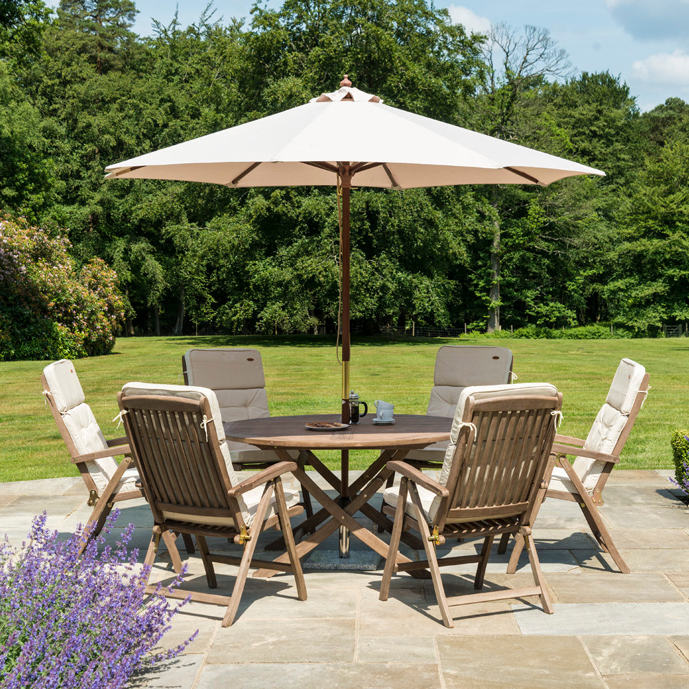 Outdoor patio set with table and 6 reclining chairs under a large parasol in a garden setting.