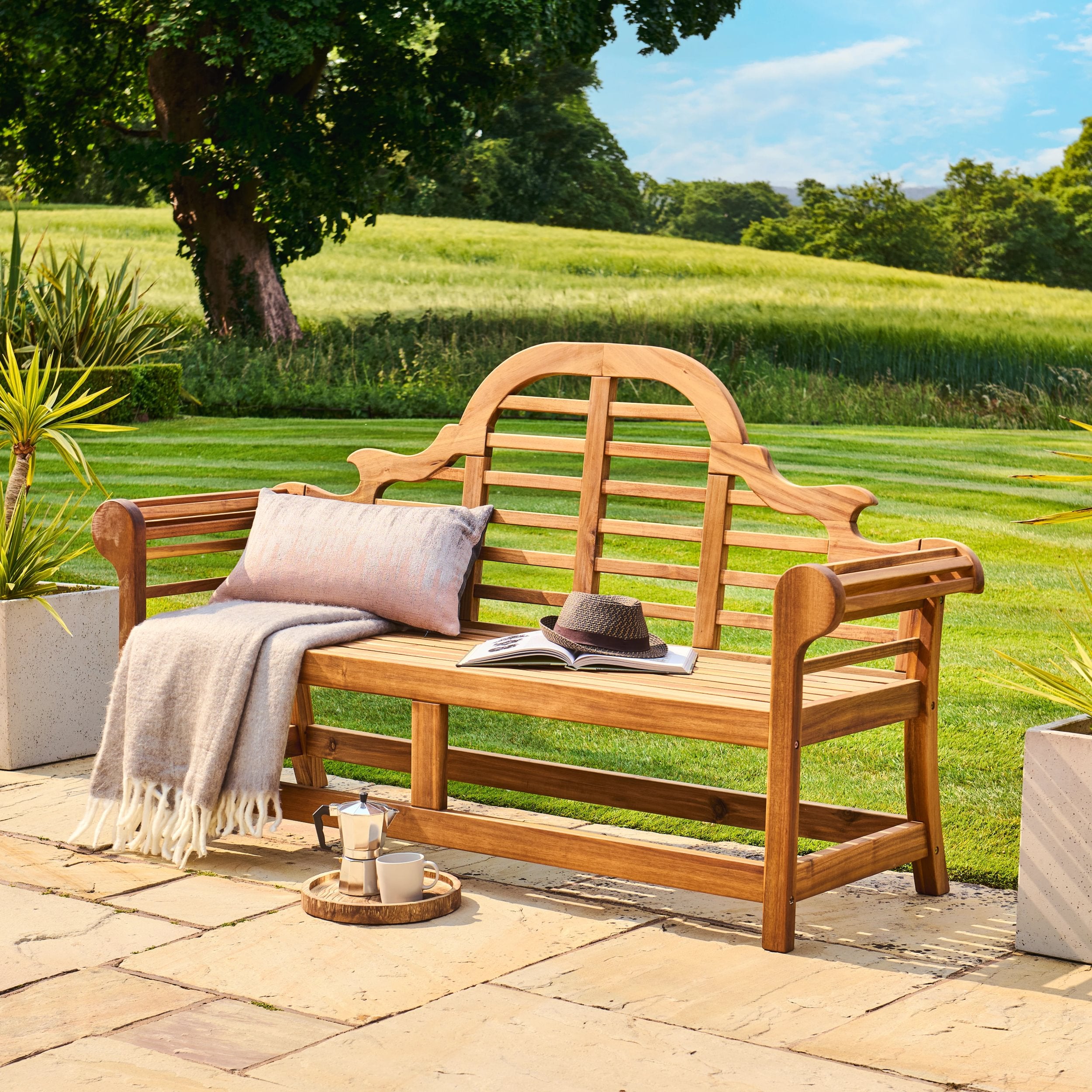 Wooden bench with cushions and a blanket in a garden setting