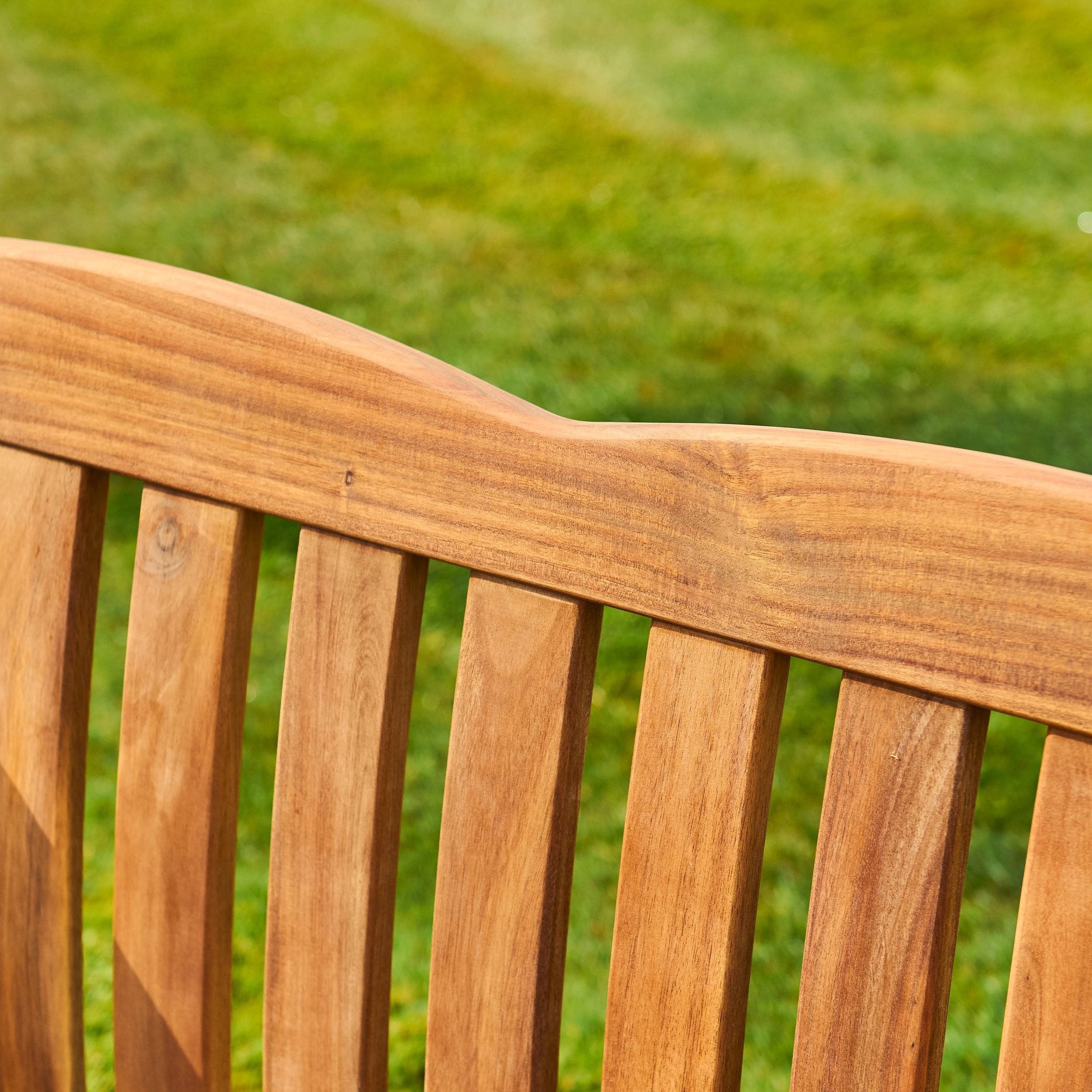 Close-up of a wooden bench with a blurred green grass background