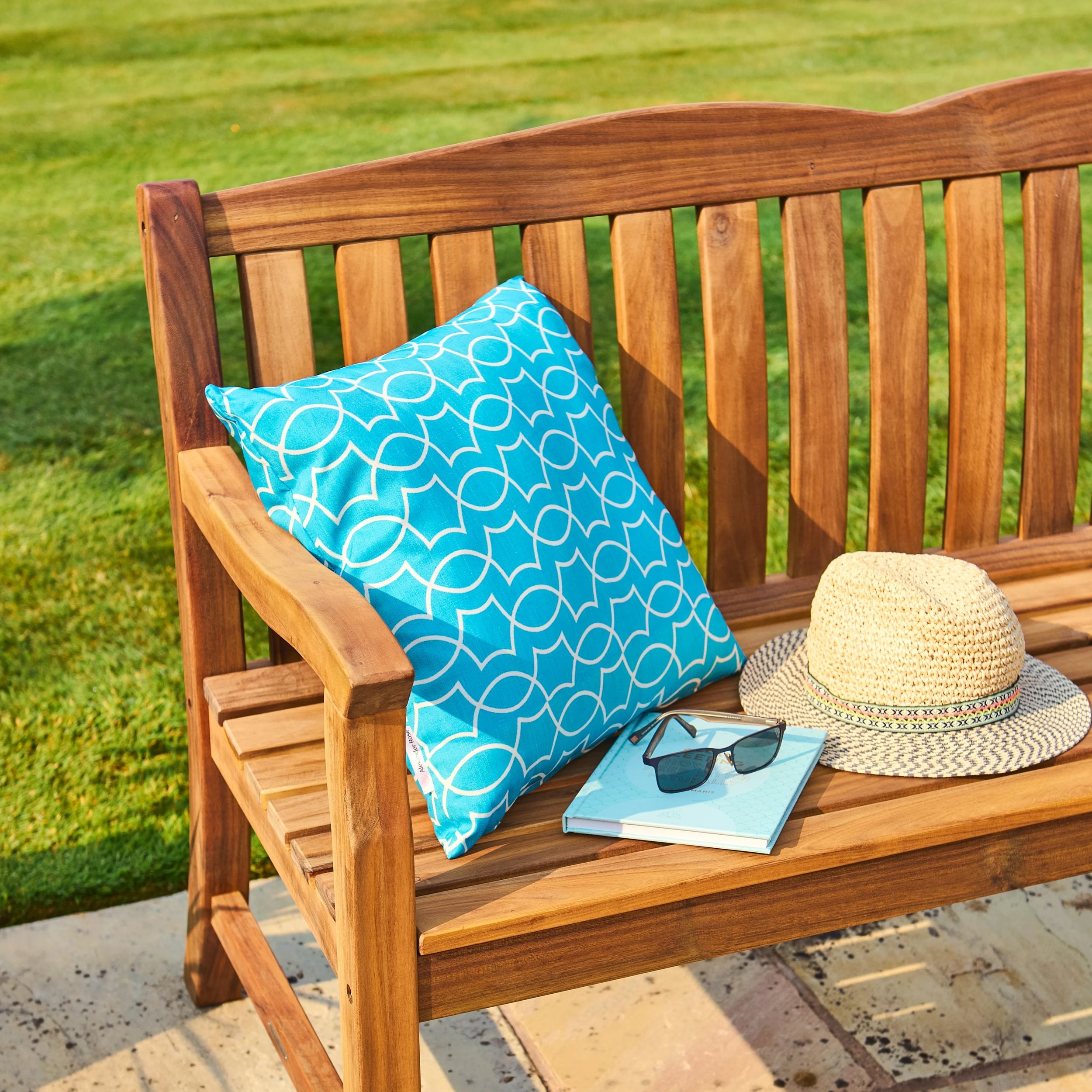 Wooden bench with a blue pillow, hat, and sunglasses on a grassy background