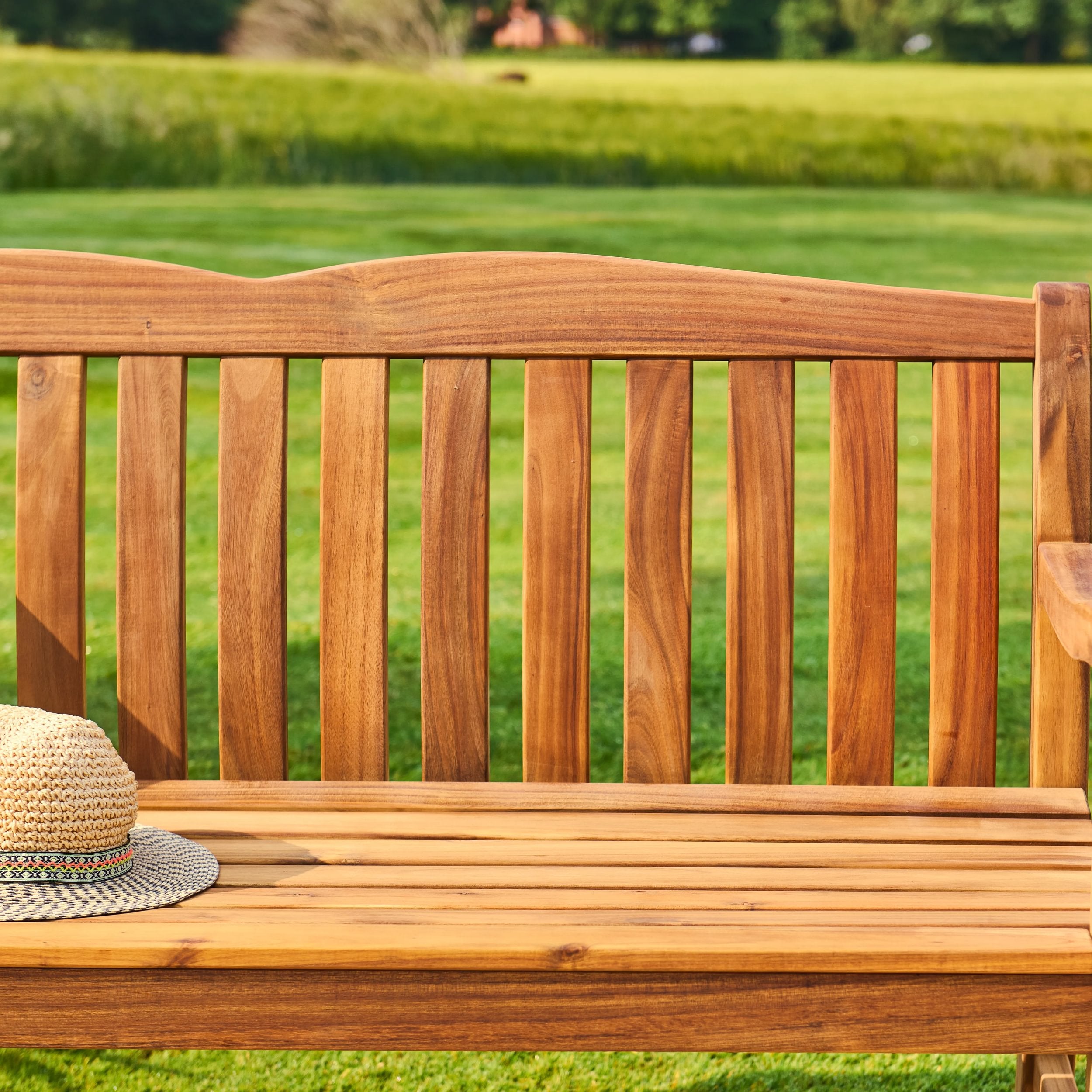 Wooden bench with a straw hat on a grassy background