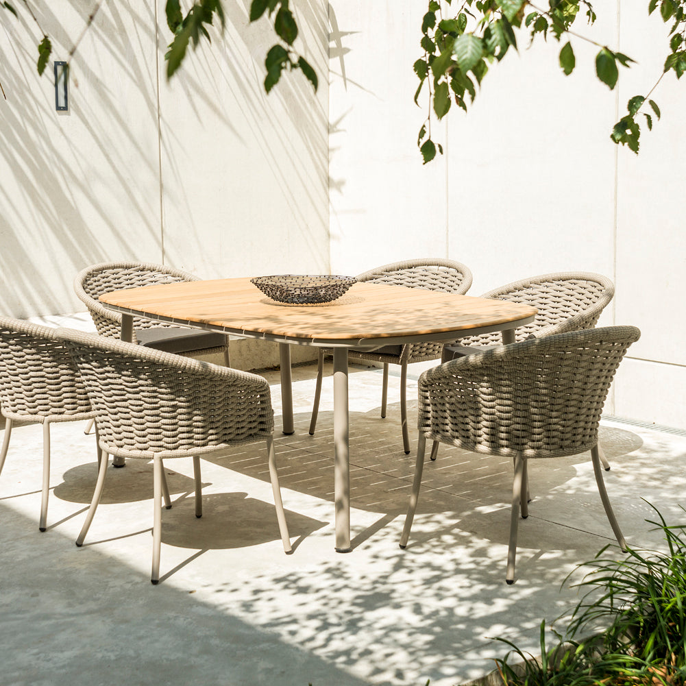 Cordial dining table with a roble wood top paired with six beige rope‑weave armchairs