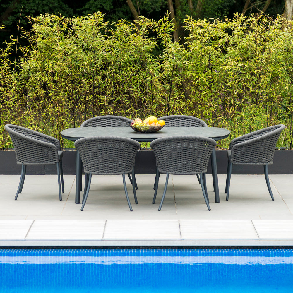 Outdoor dining set for six by a pool with a hedge in the background
