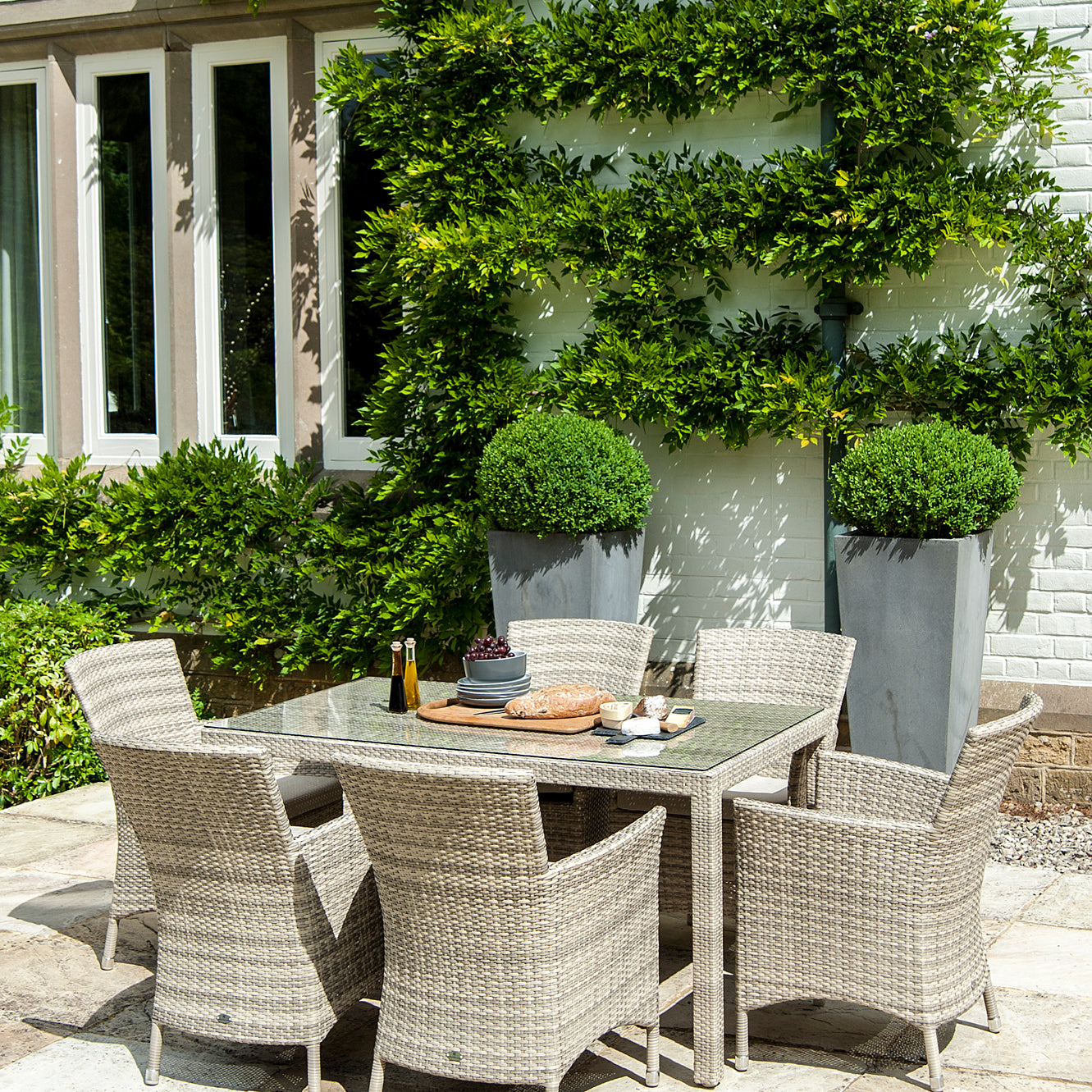 Outdoor dining area with 6 rattan armchairs and a table in front of a white house with climbing plants