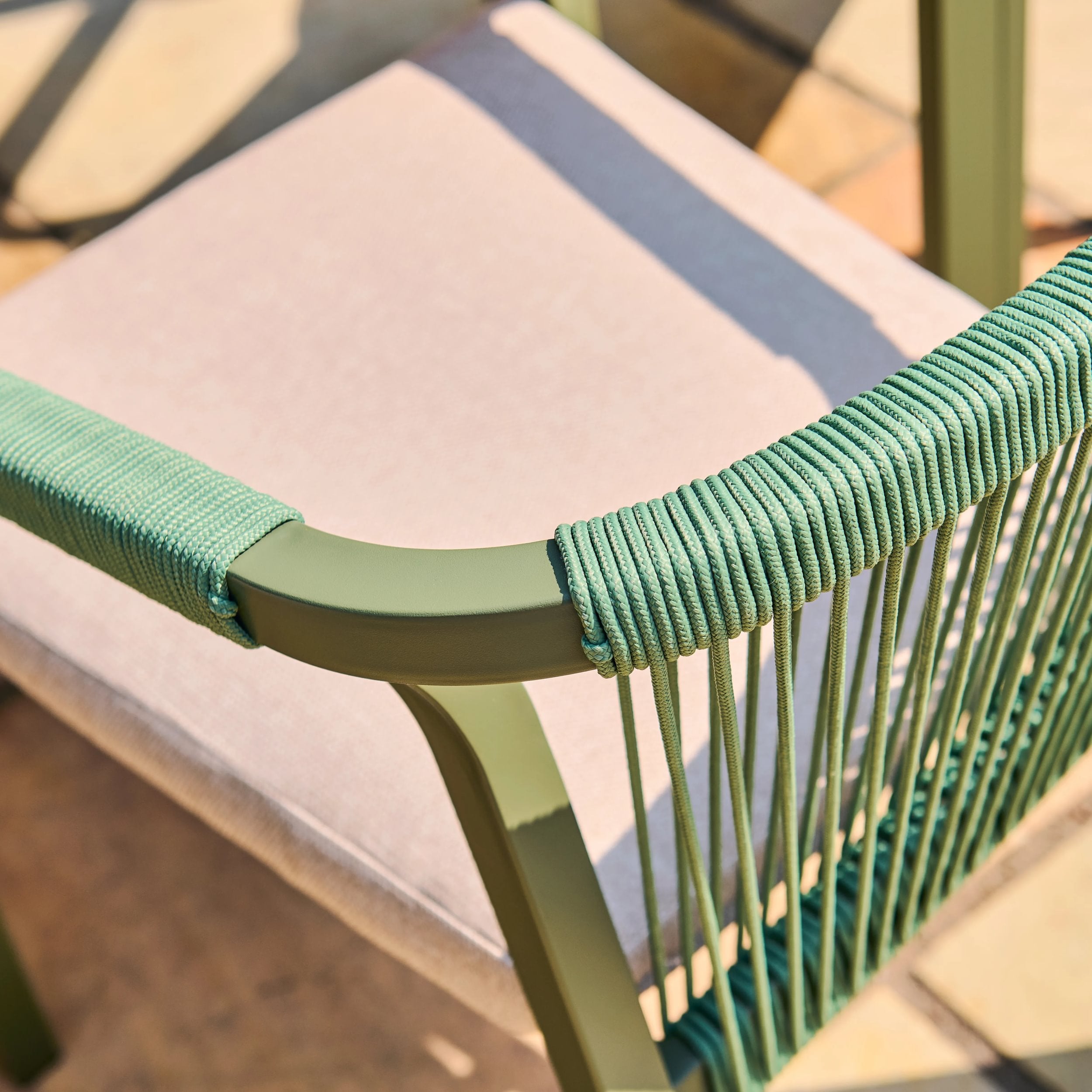 Close-up of a chair with green woven backrest and pink cushion.