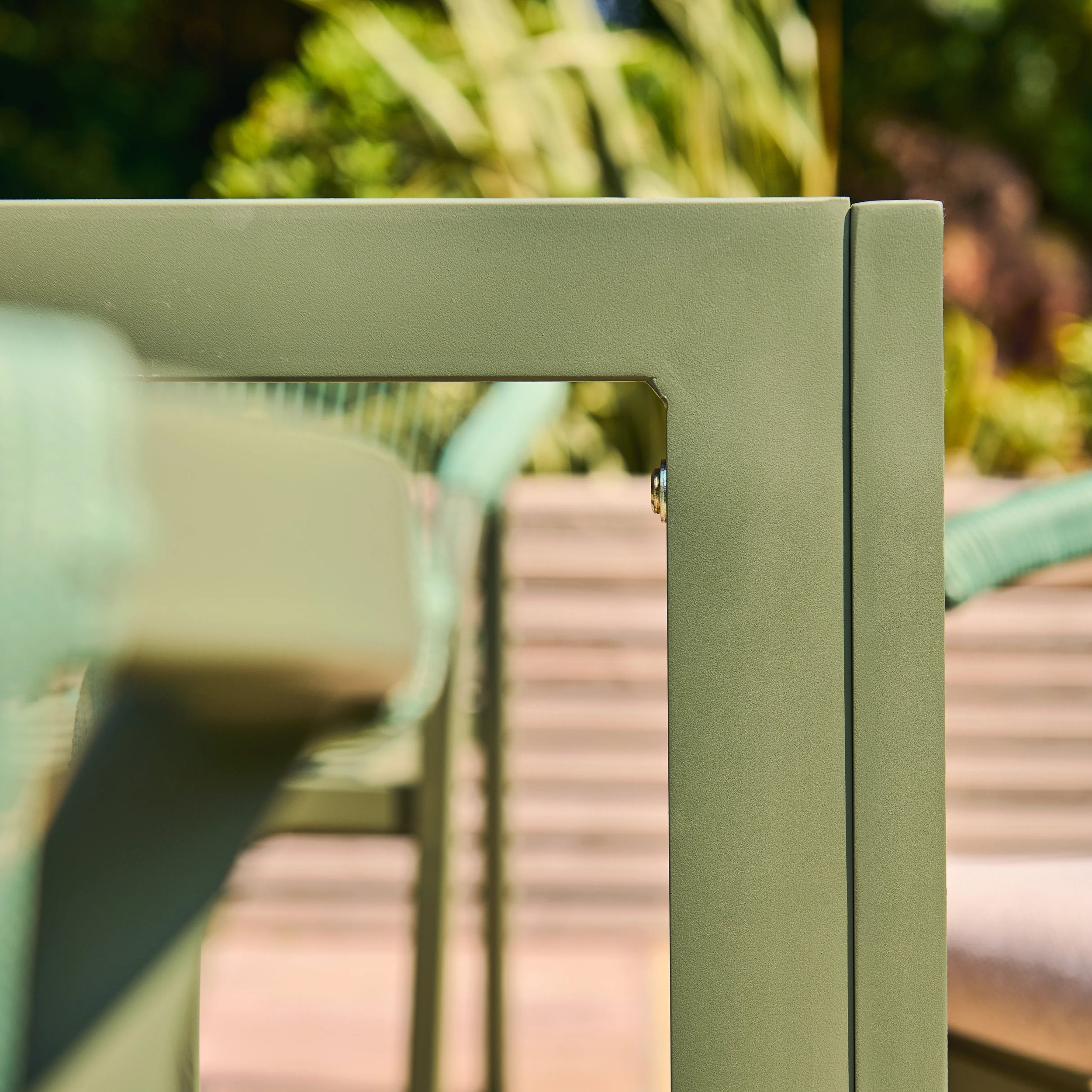 Close-up of a green metal chair frame with blurred outdoor background