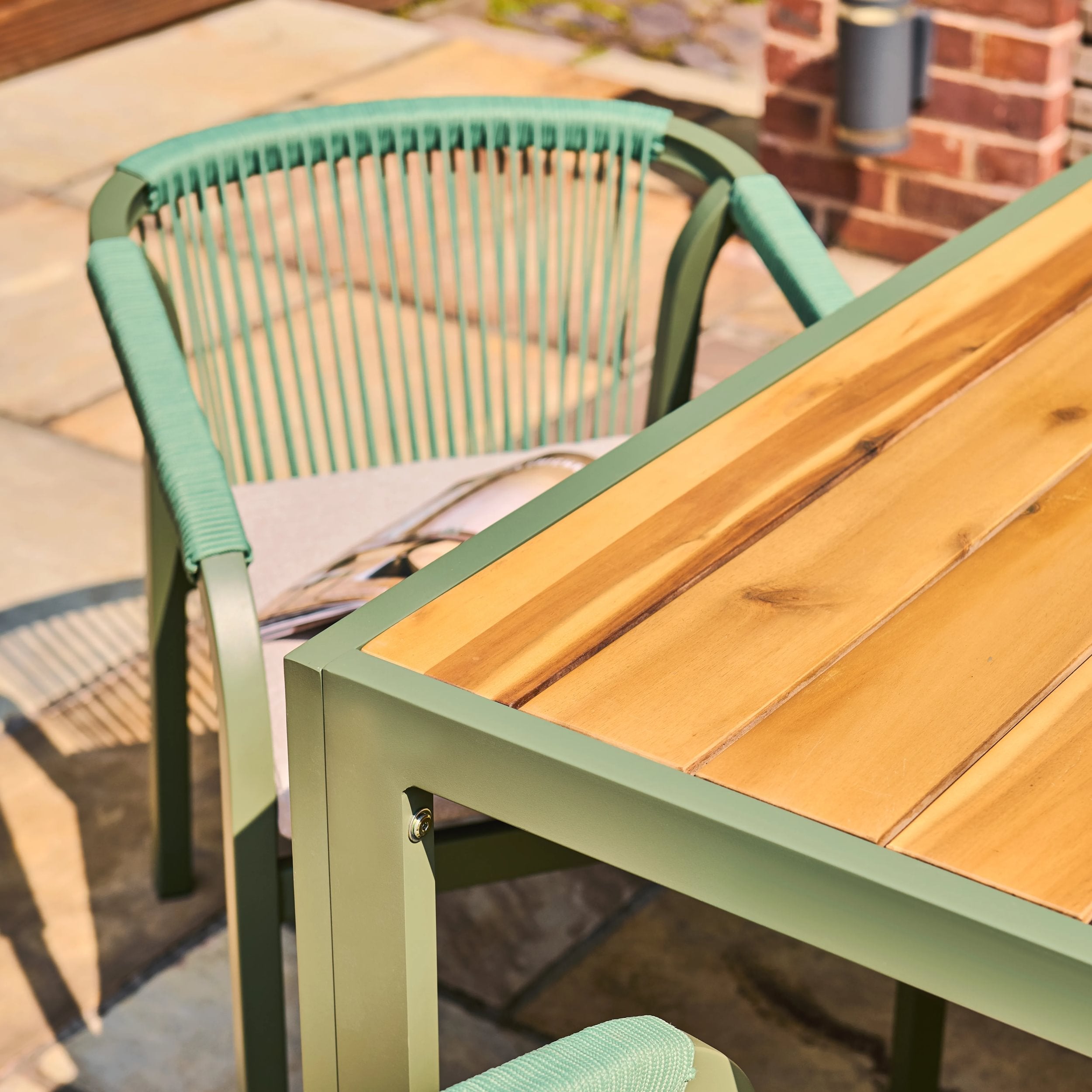 Timber table with green metal frame and chair on a patio