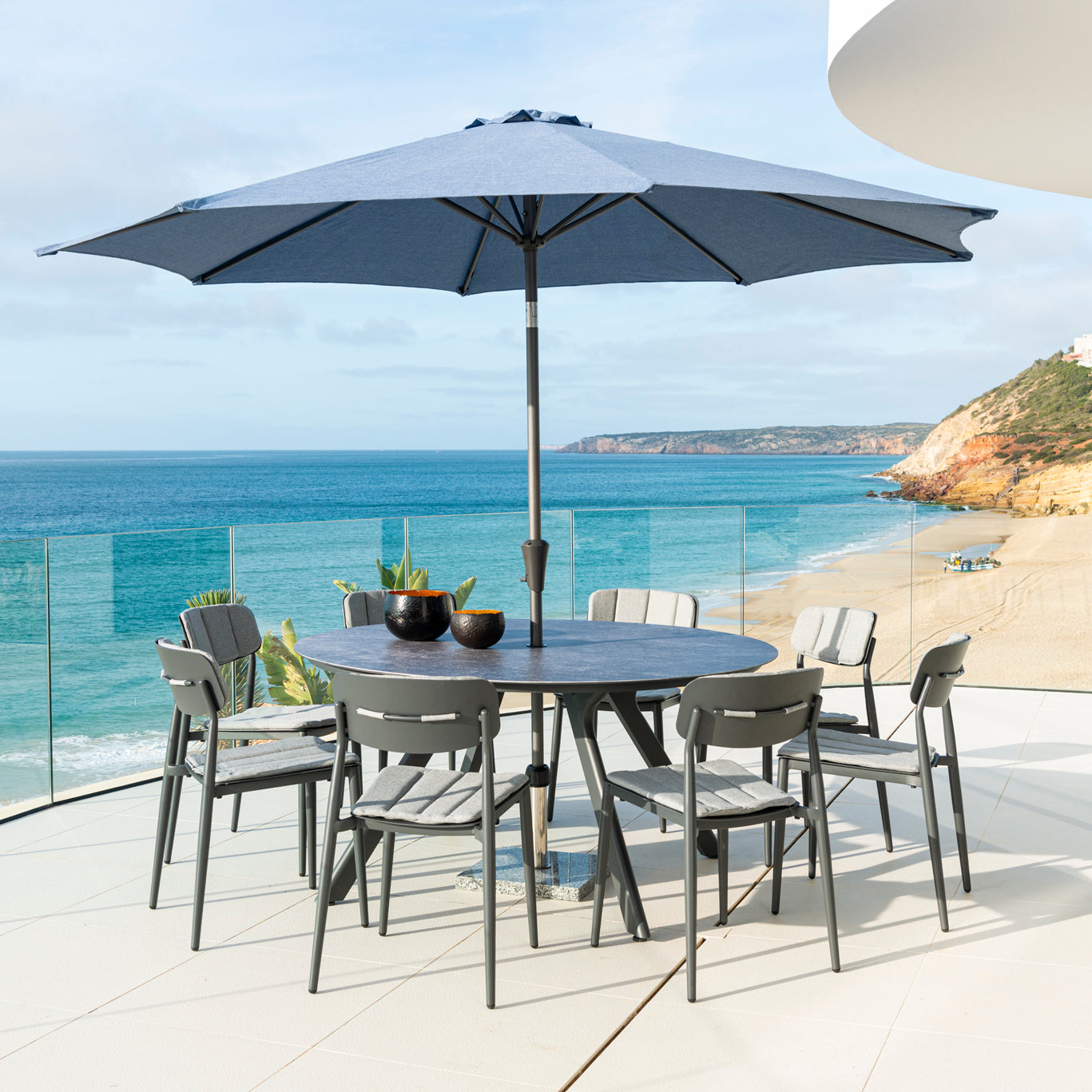 Outdoor dining set with umbrella on a balcony overlooking the ocean.