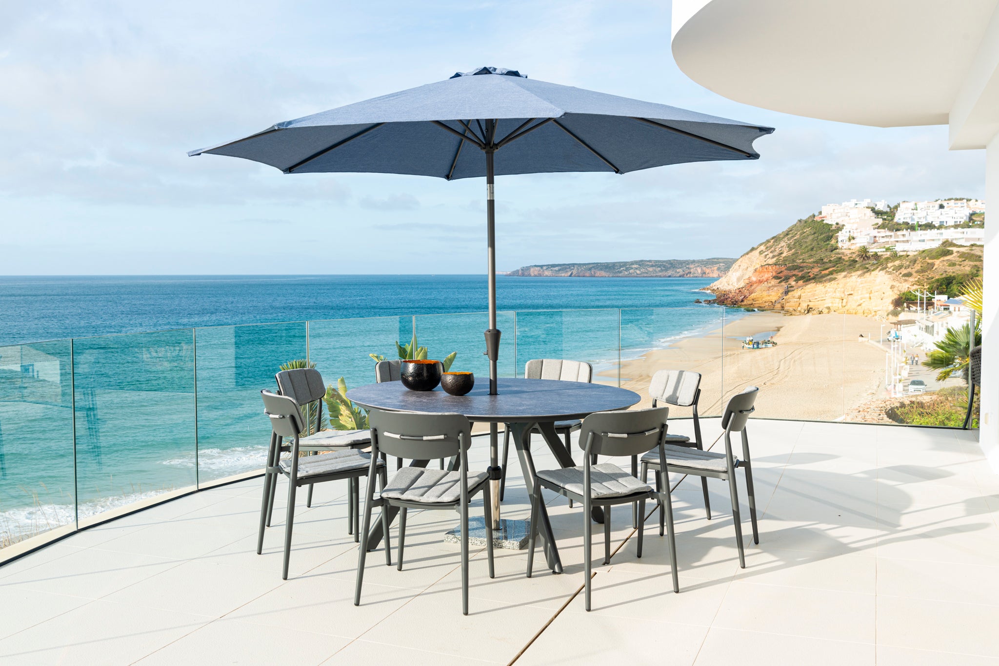 Outdoor dining set with umbrella on a balcony overlooking the ocean.