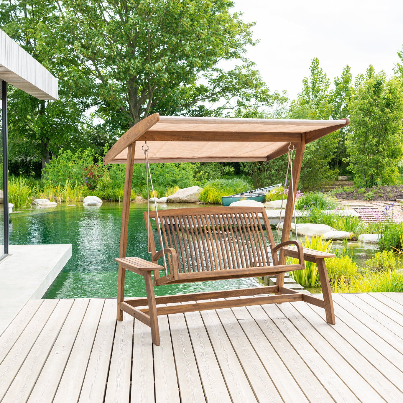 Wooden swing chair with canopy on a wooden deck by a poolside.