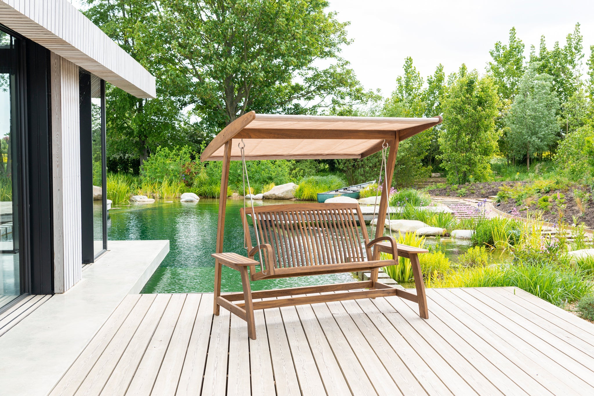 Wooden swing chair with canopy on a wooden deck by a poolside.