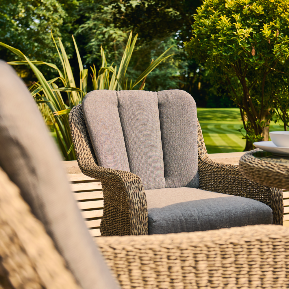 Grey cushioned outdoor chair with wicker frame in a garden setting