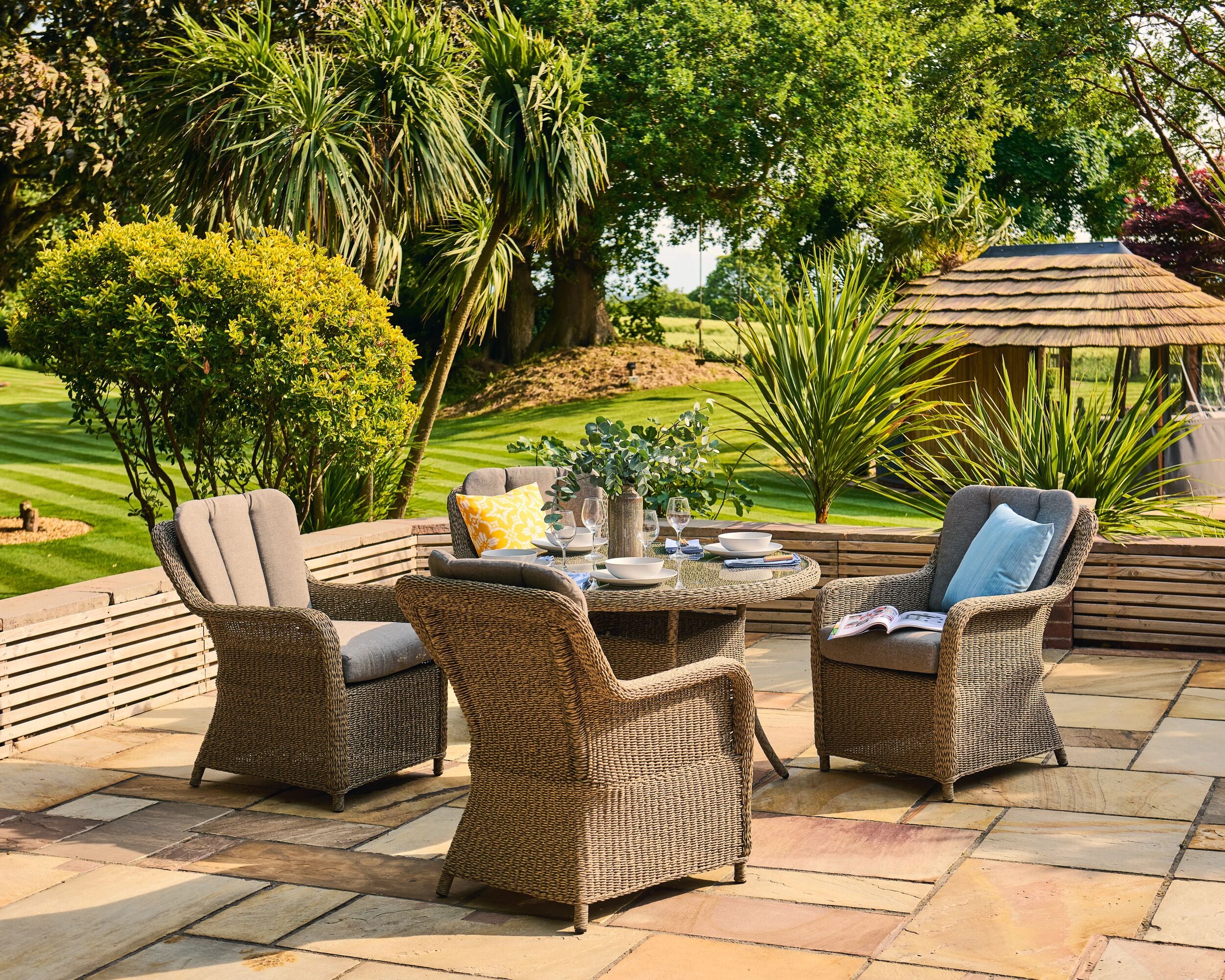Outdoor patio set with chairs and a table on a stone patio, surrounded by greenery.