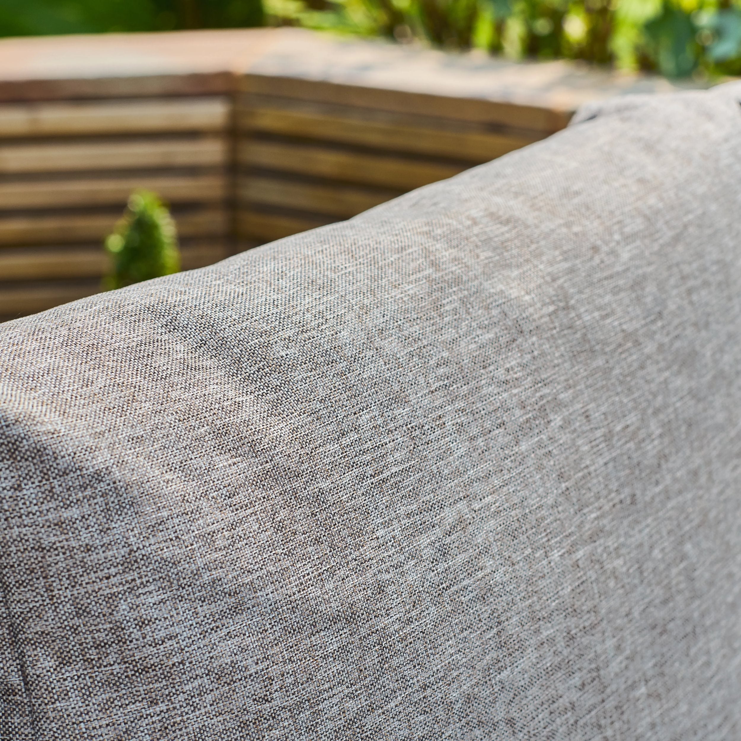 Close-up of a textured gray fabric surface with a blurred wooden structure and greenery in the background.