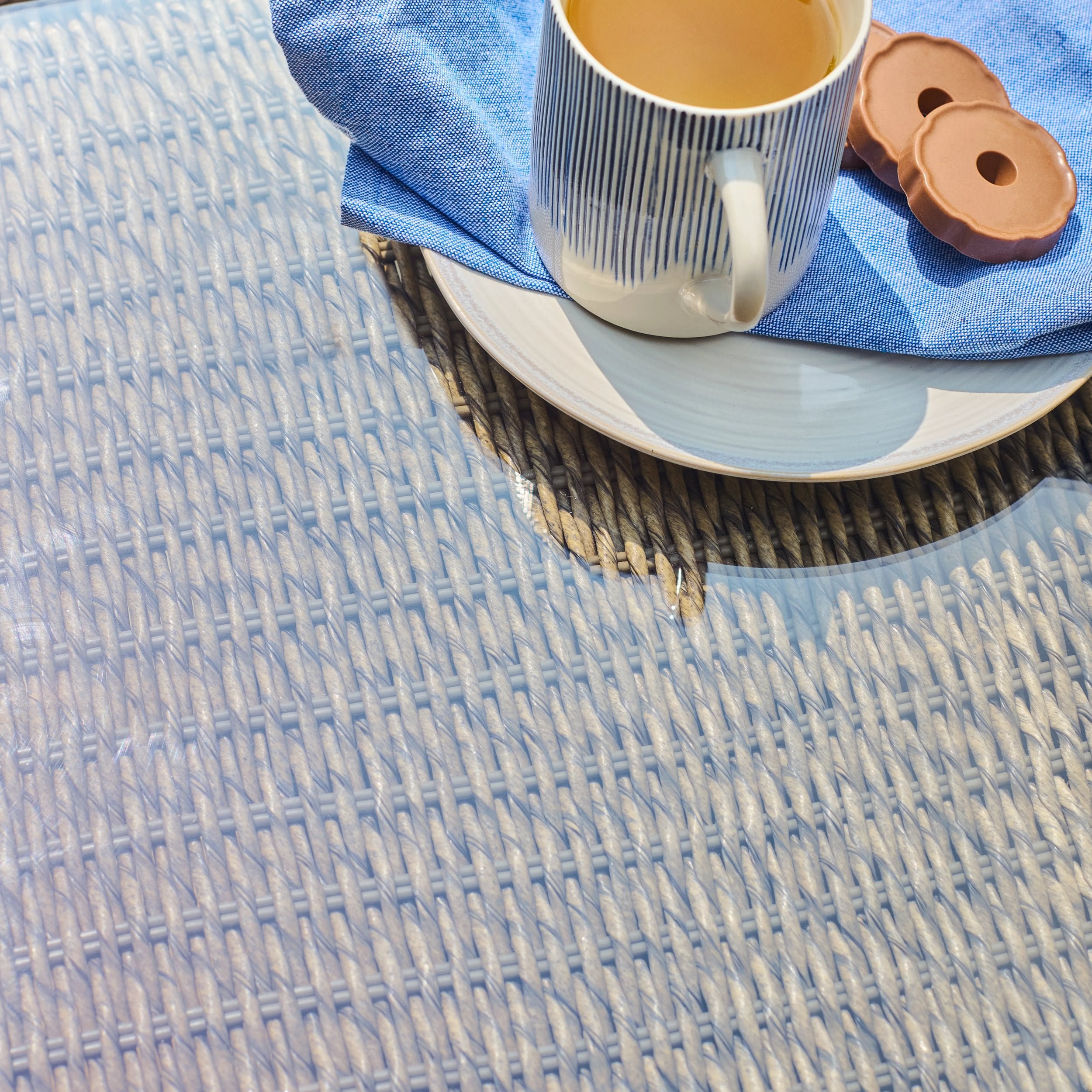 glass top woven table with a cup, saucer, and cookies on a plate
