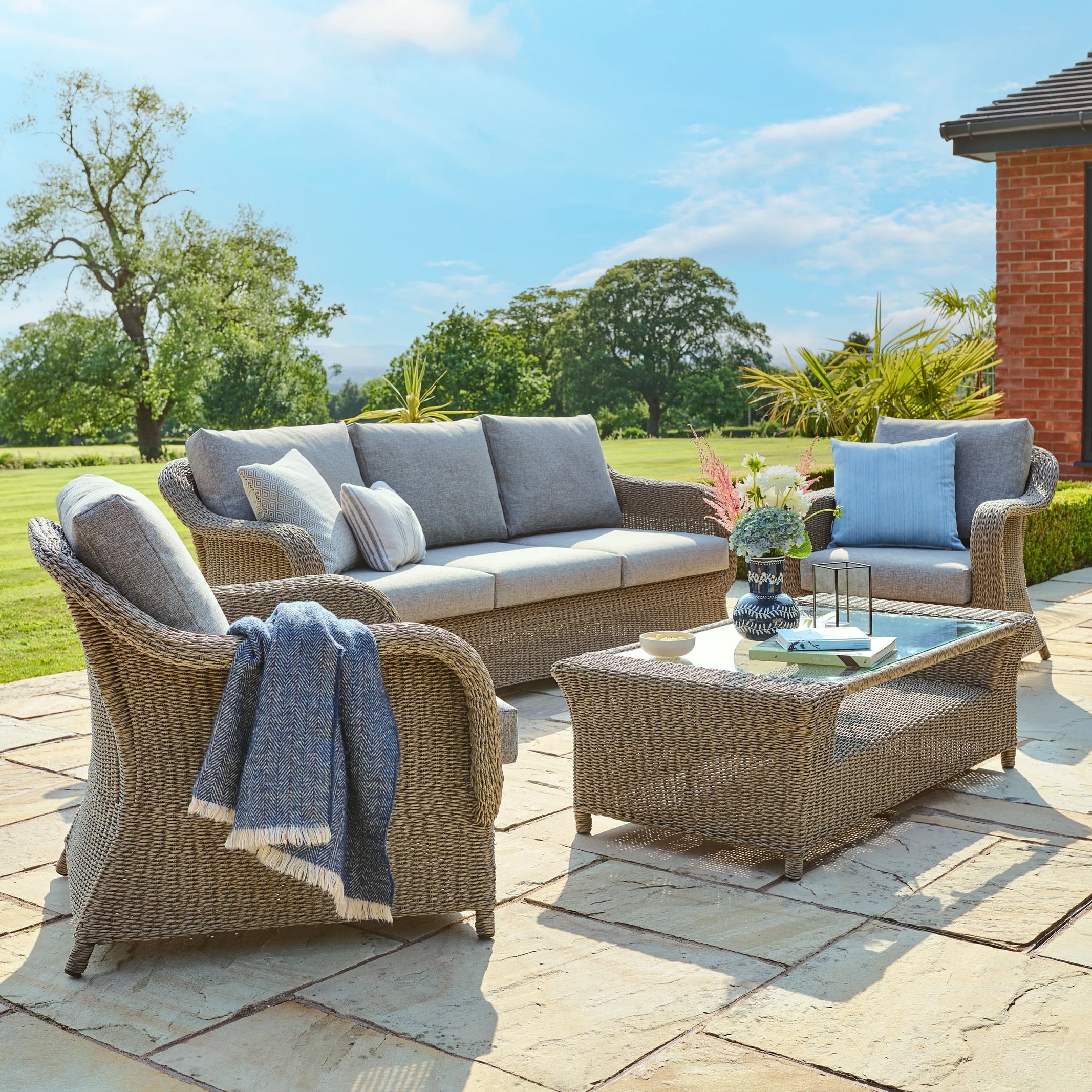 Outdoor patio set with wicker furniture and cushions on a stone patio.
