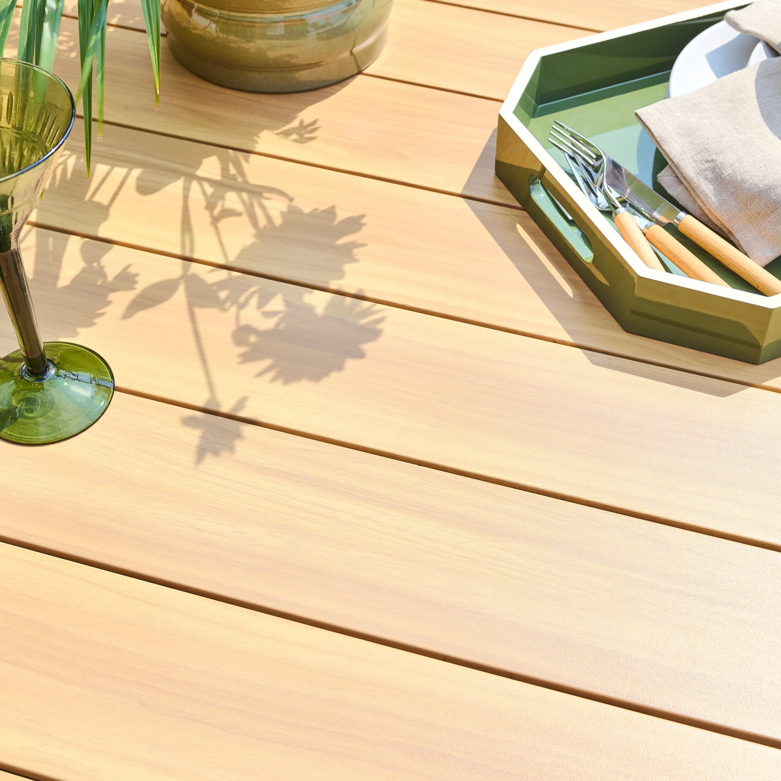 Wood effect table top with a green tray containing cutlery and a glass on the surface.