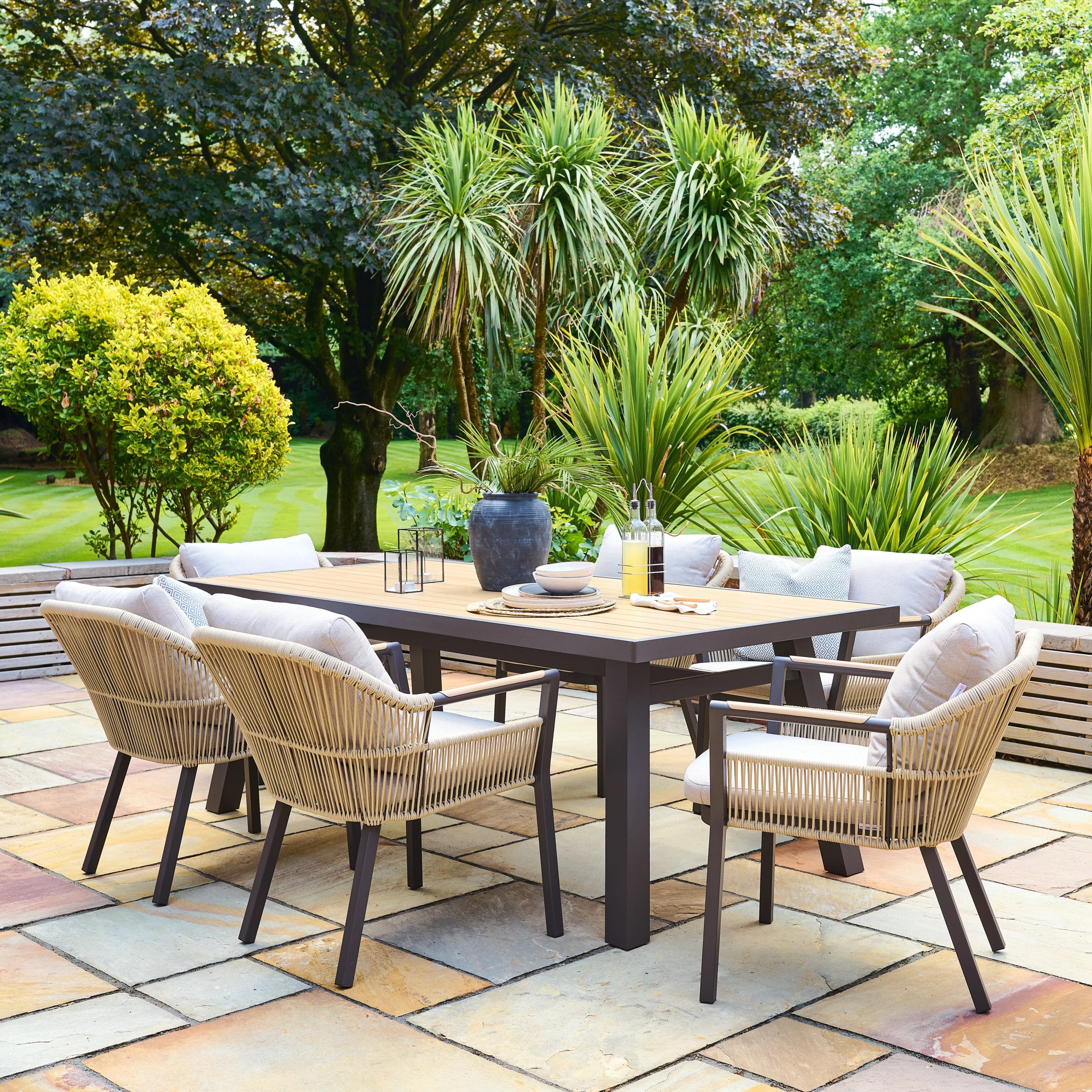 Outdoor patio set with table and chairs on a stone patio, surrounded by greenery.