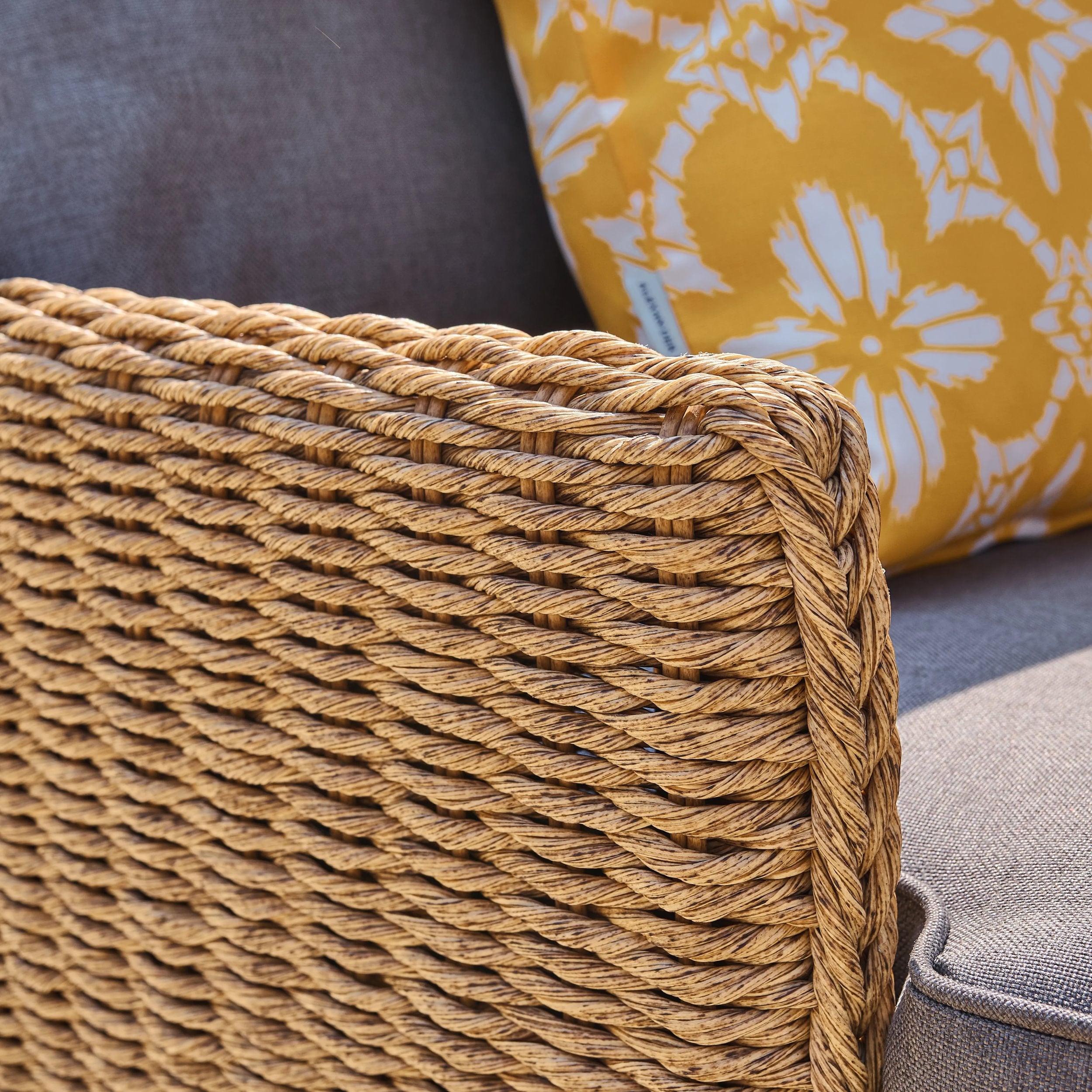 Close-up of a woven armchair with a floral-patterned pillow in the background